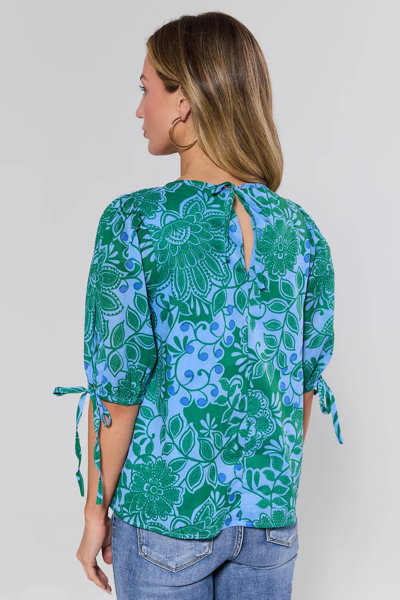 Woman wearing a green and blue floral patterned top with a plain background