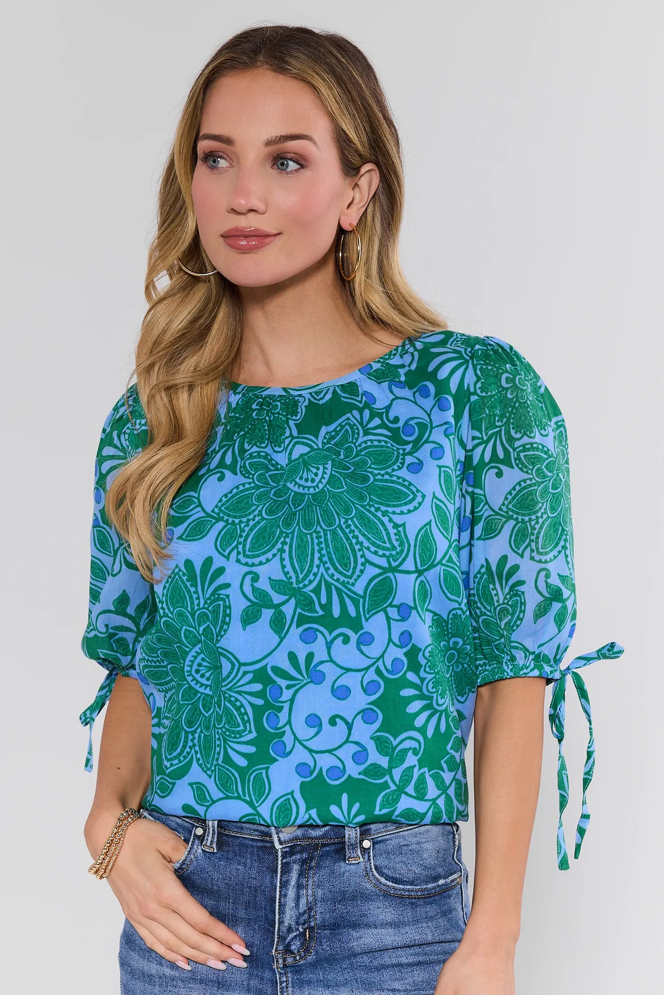 Woman wearing a blue and green floral patterned top with a plain background