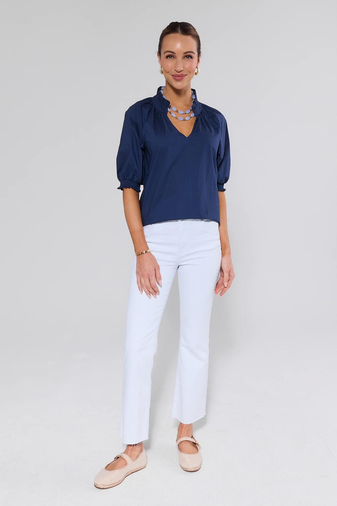 Woman wearing a navy blue blouse and white pants on a plain background