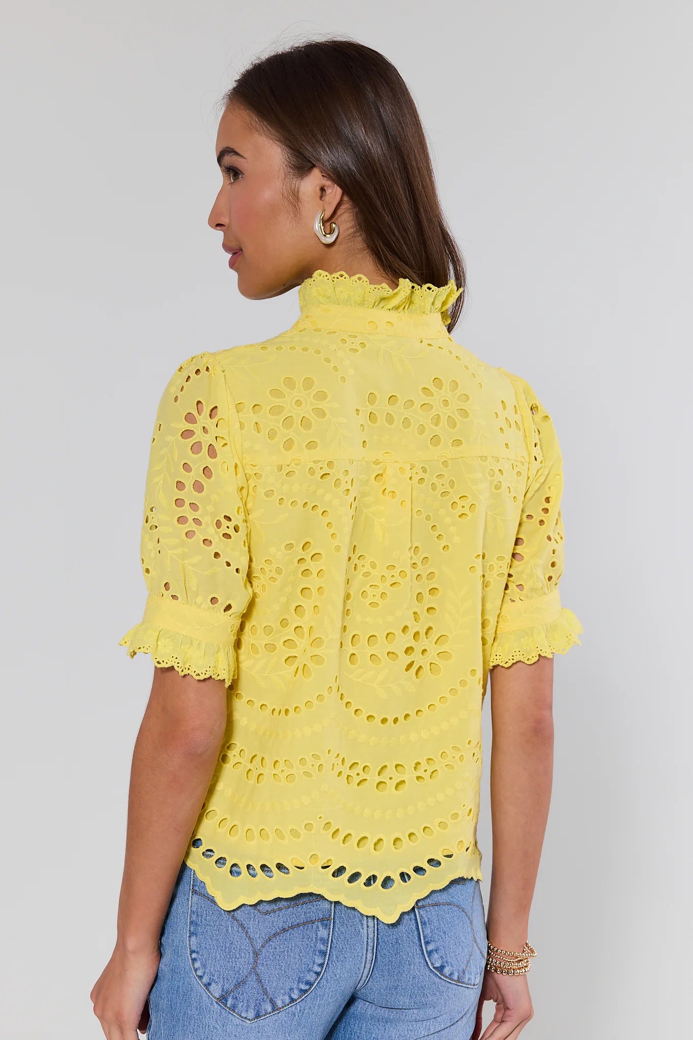 Woman wearing a yellow lace top against a plain background
