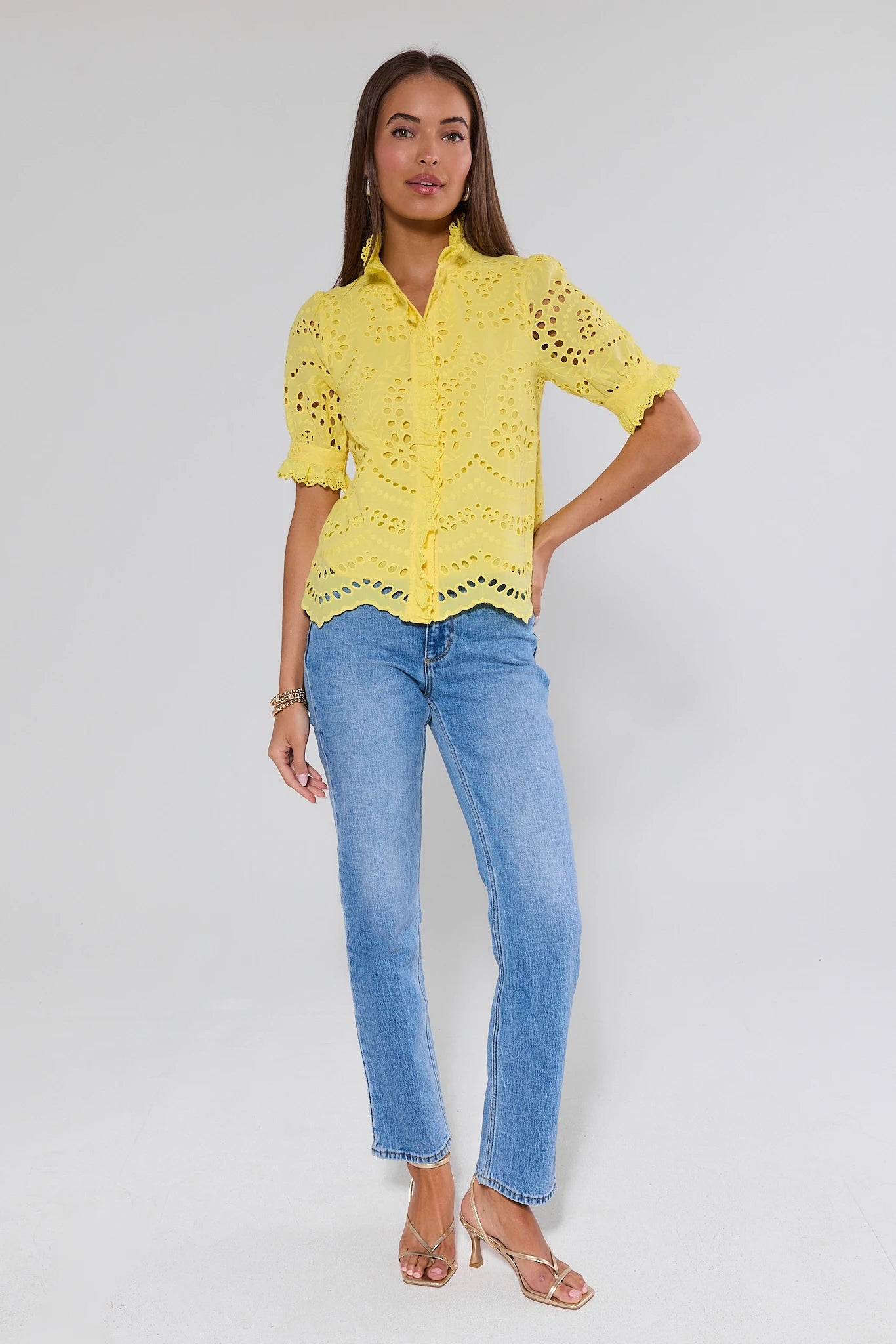Woman wearing a yellow lace blouse and blue jeans on a white background