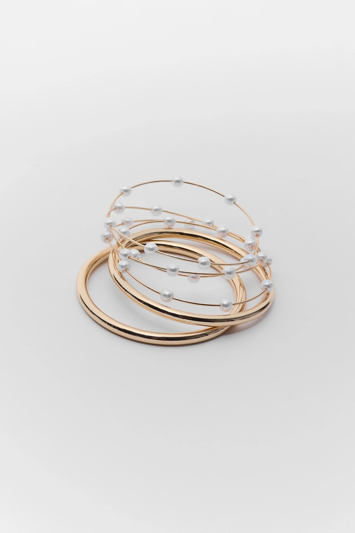 Set of gold bangles with beaded detailing on a light gray background