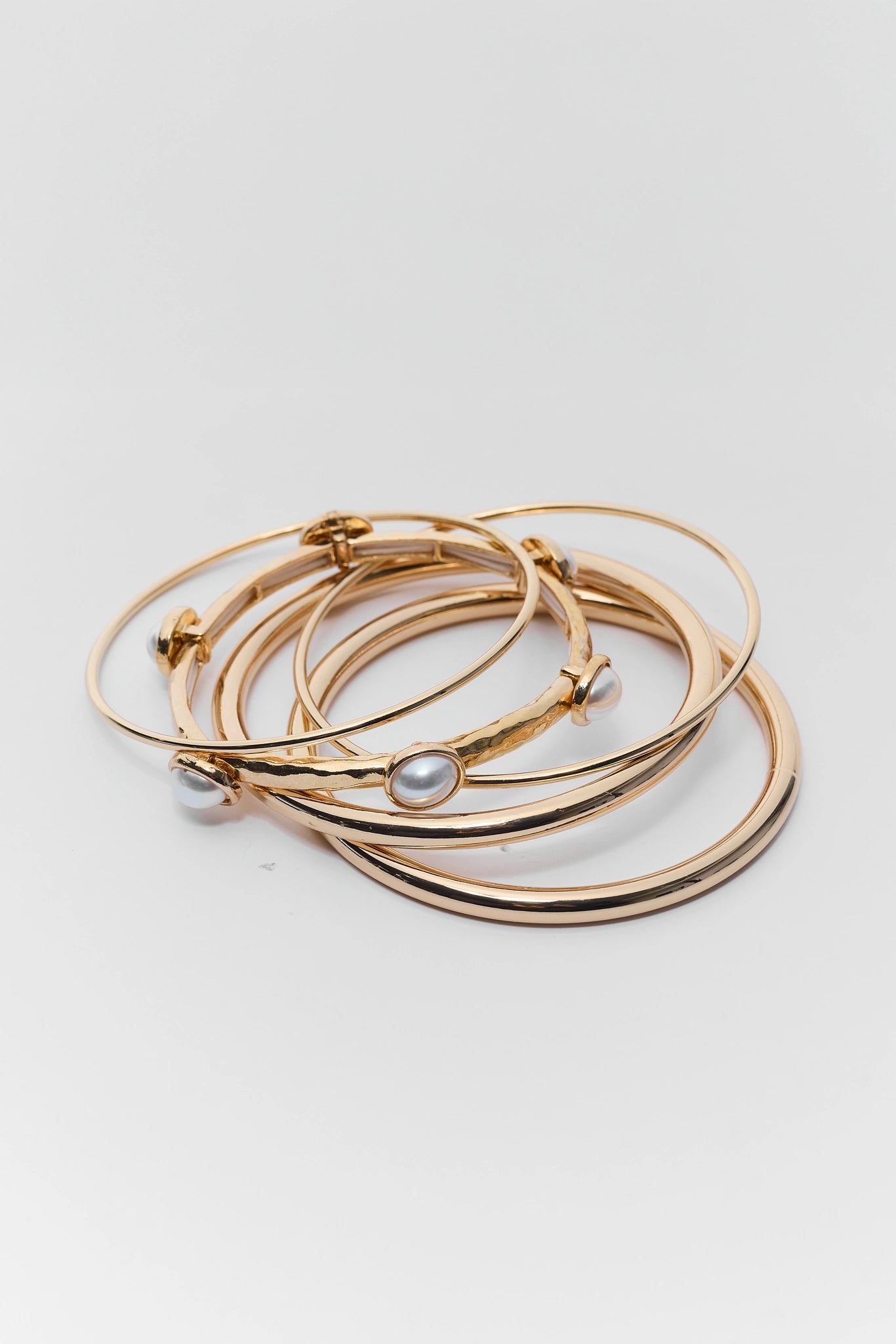 Stack of gold bangles with pearl accents on a light gray background