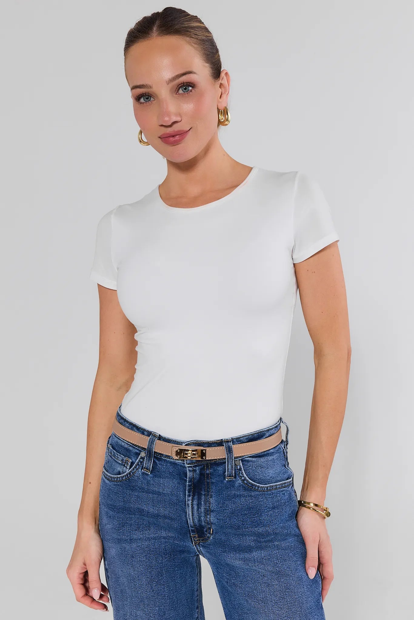 Woman wearing a white t-shirt and blue jeans against a plain background