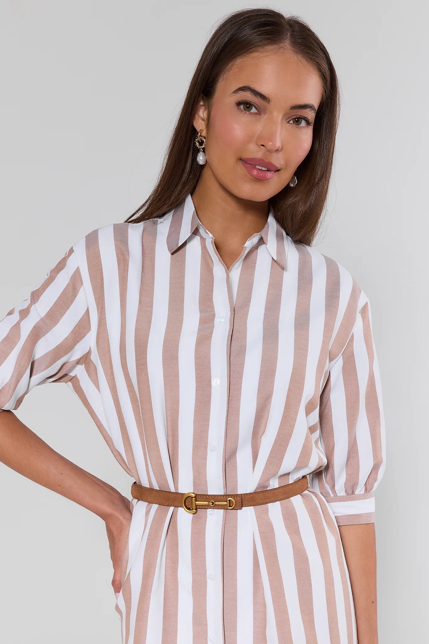 Woman wearing a striped shirt dress with a belt against a plain background