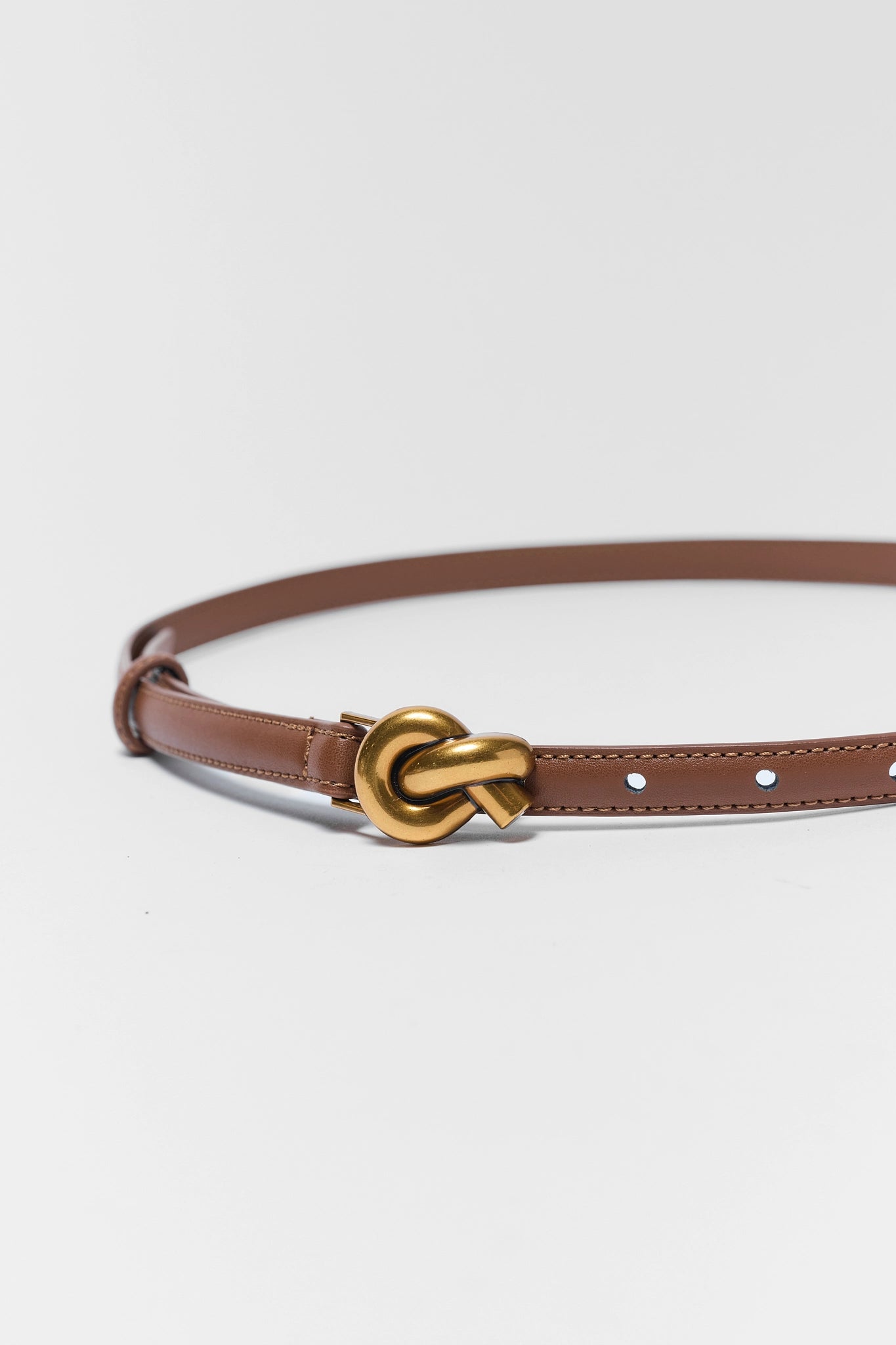 close up Brown belt with a gold knot buckle on a light gray background