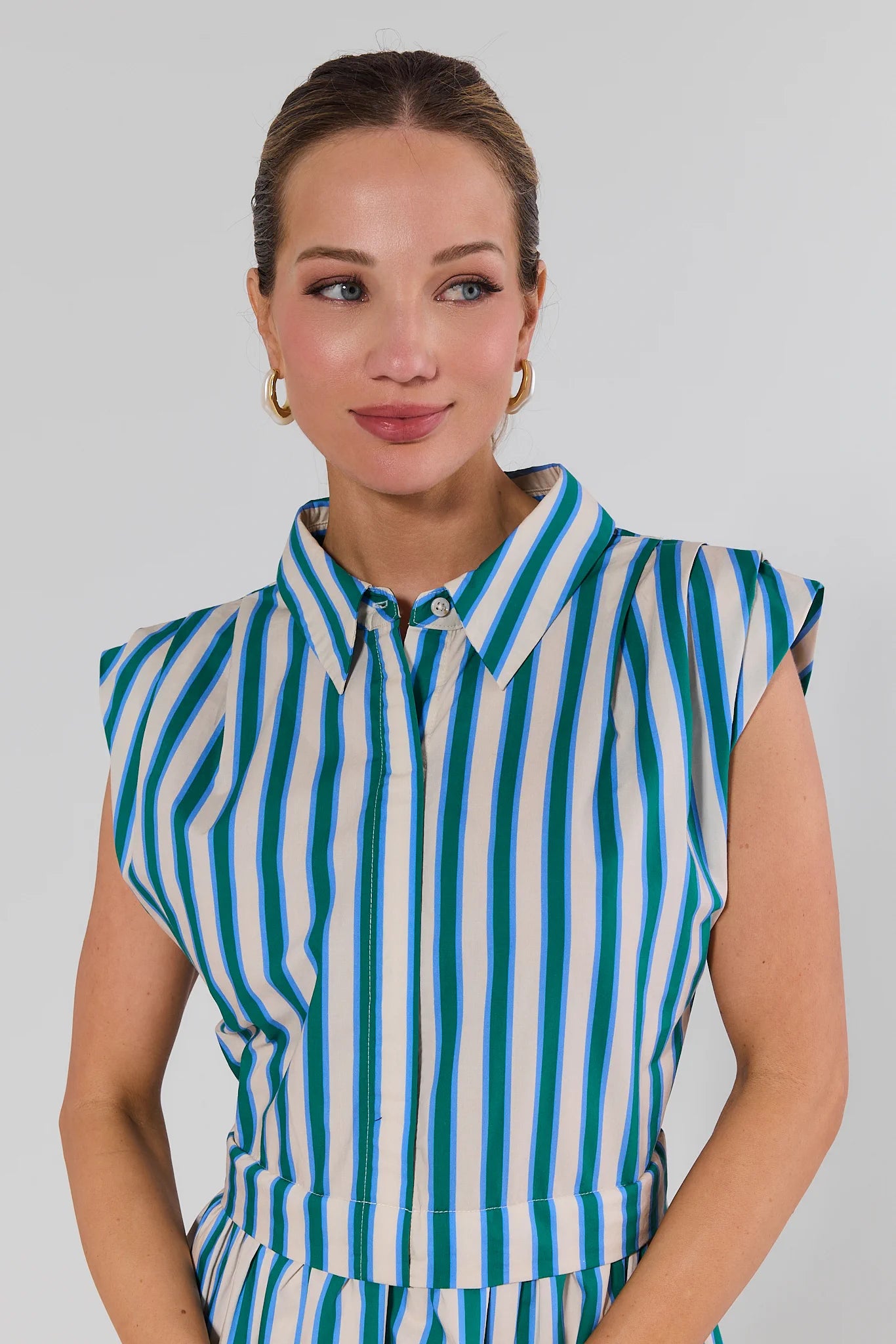 Woman wearing a sleeveless striped shirt with green and white vertical stripes on a plain background