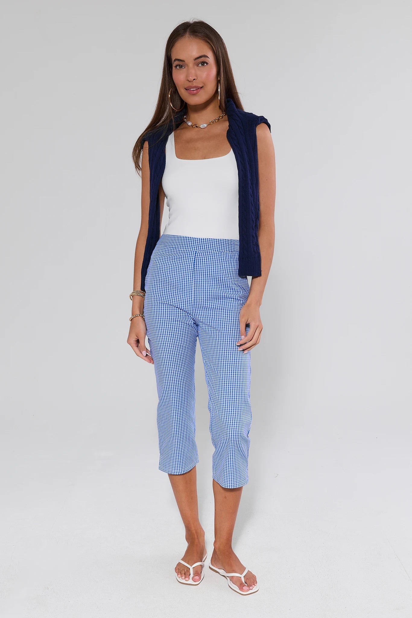 Woman wearing a white top, navy cardigan, and blue checkered pants on a light gray background