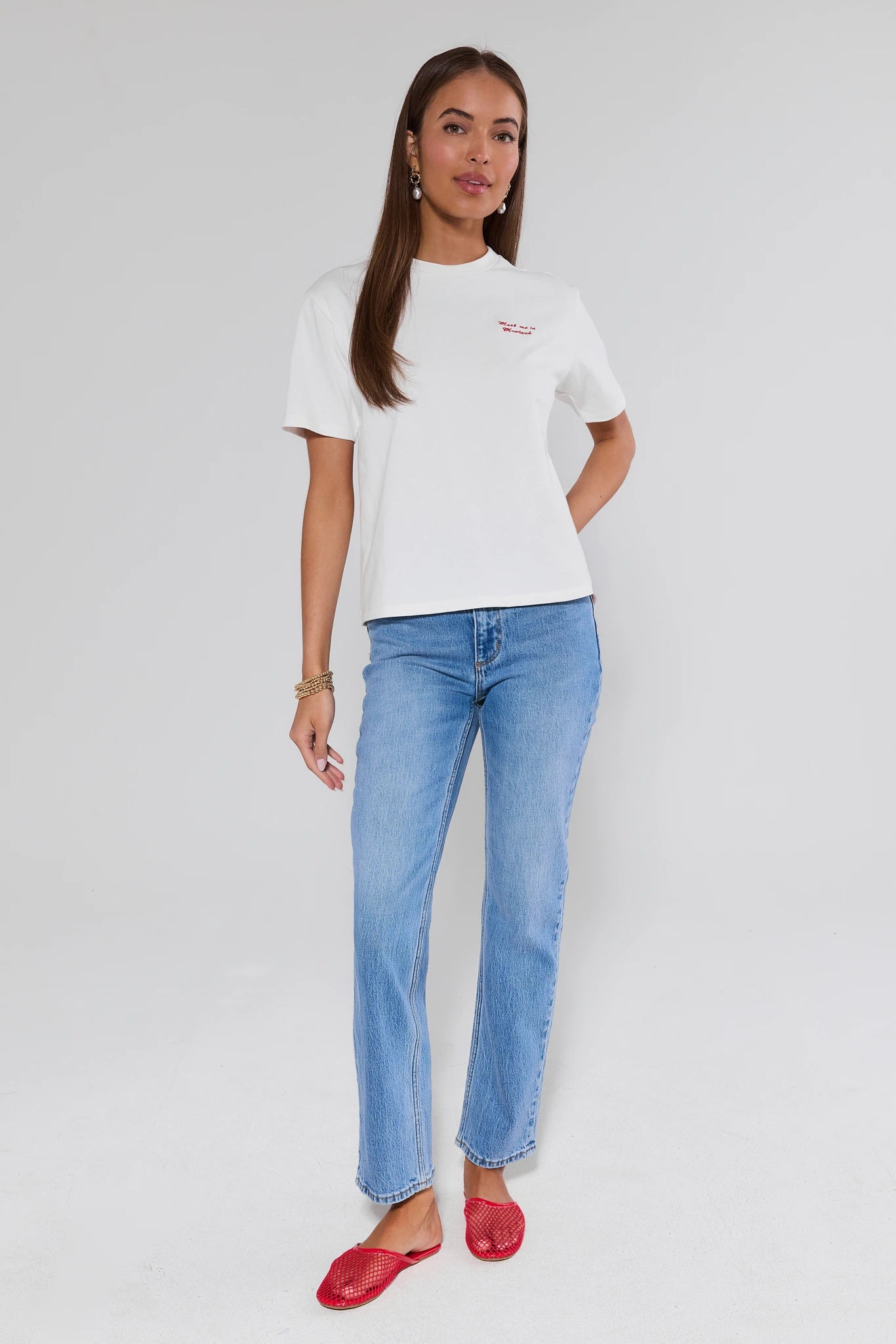 Woman wearing a white t-shirt and blue jeans with red shoes on a plain background