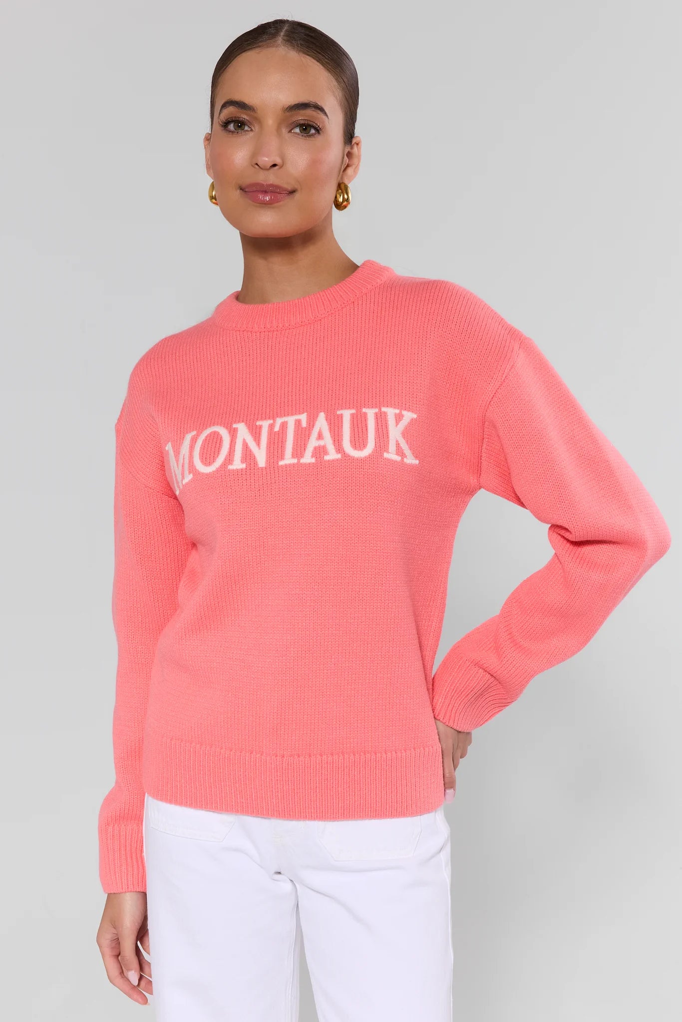 Woman wearing a coral sweater with 'Montauk' text on a plain background