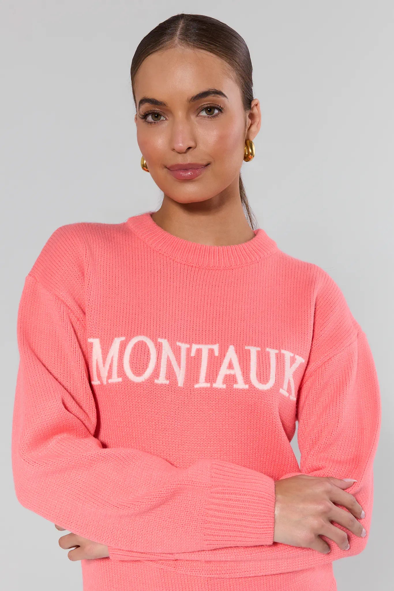 Woman wearing a pink sweater with 'Montauk' text on a gray background