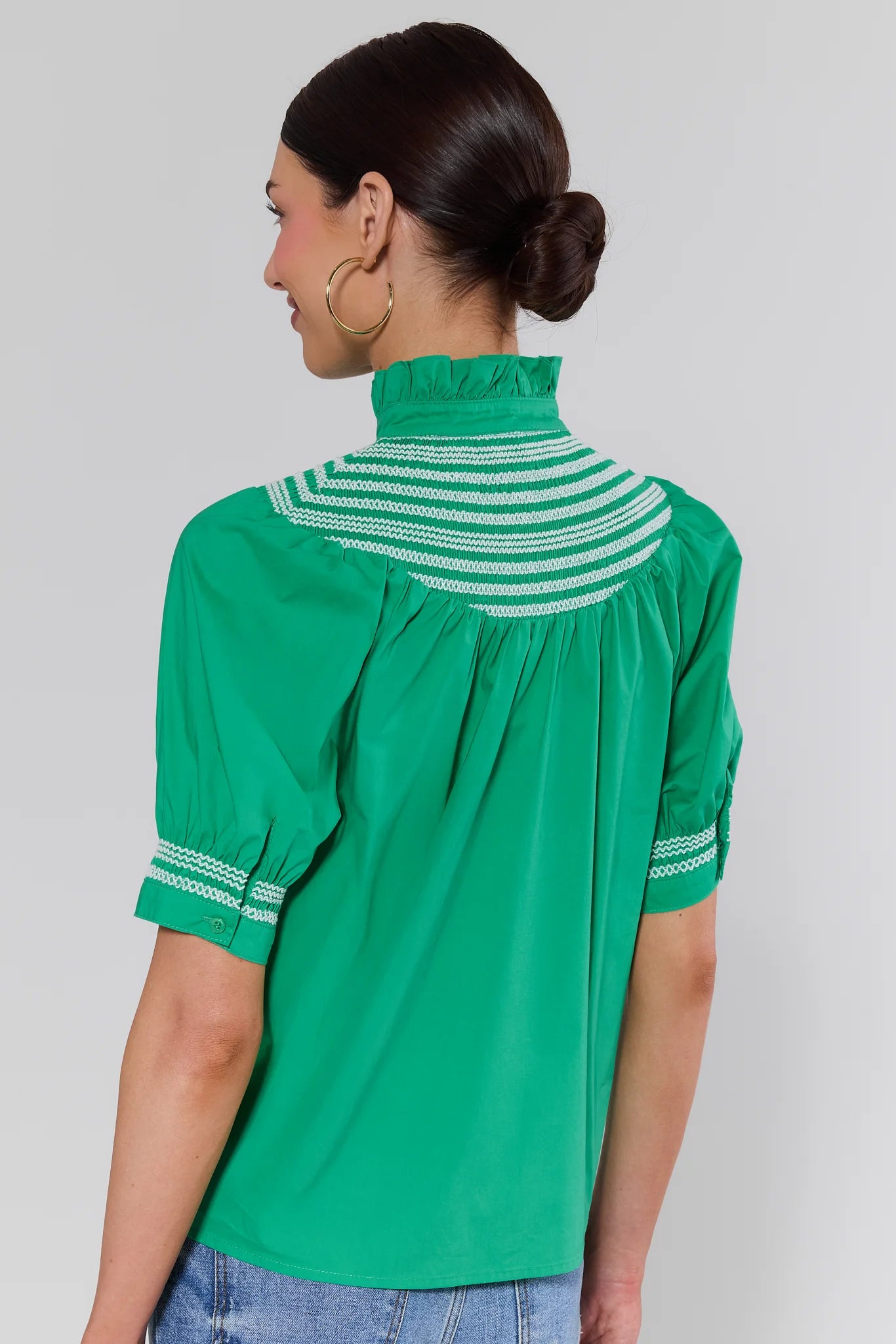 Green blouse with white striped details worn by a person on a plain background