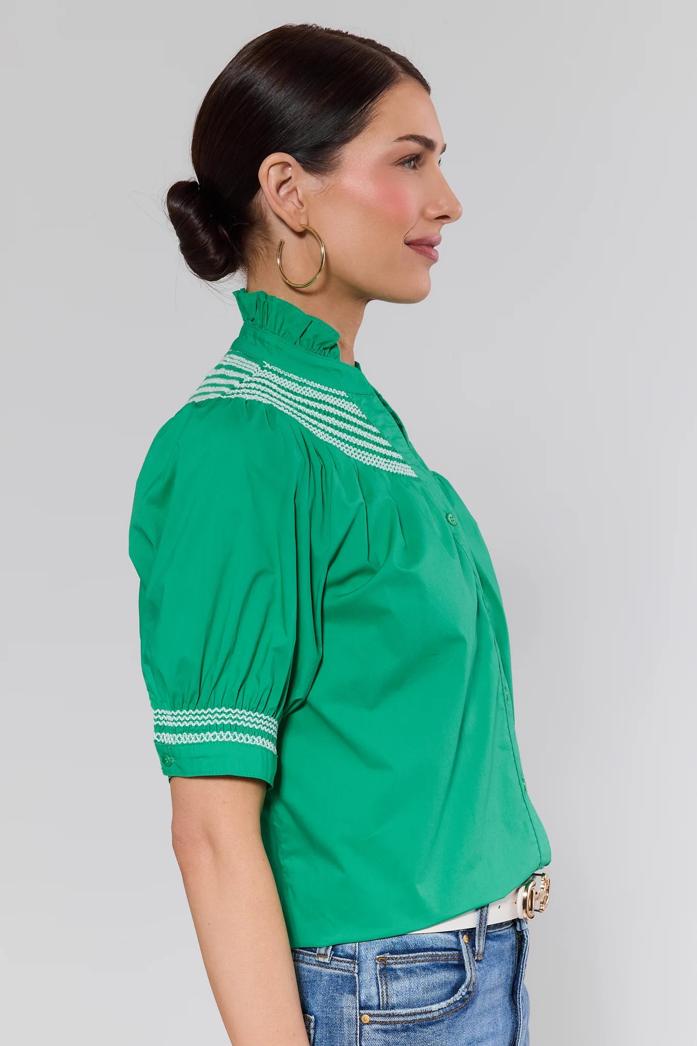 side shot Woman wearing a green blouse with white patterns on a plain background