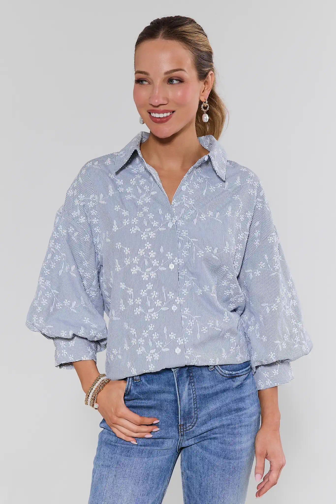 Woman wearing a light blue floral blouse and jeans against a plain background