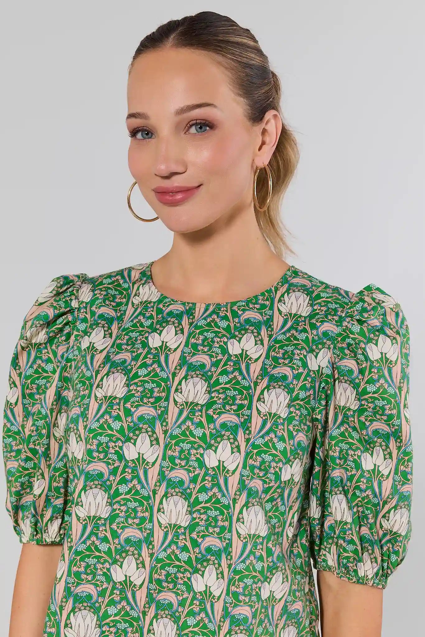 Woman close up wearing a green floral dress against a plain background
