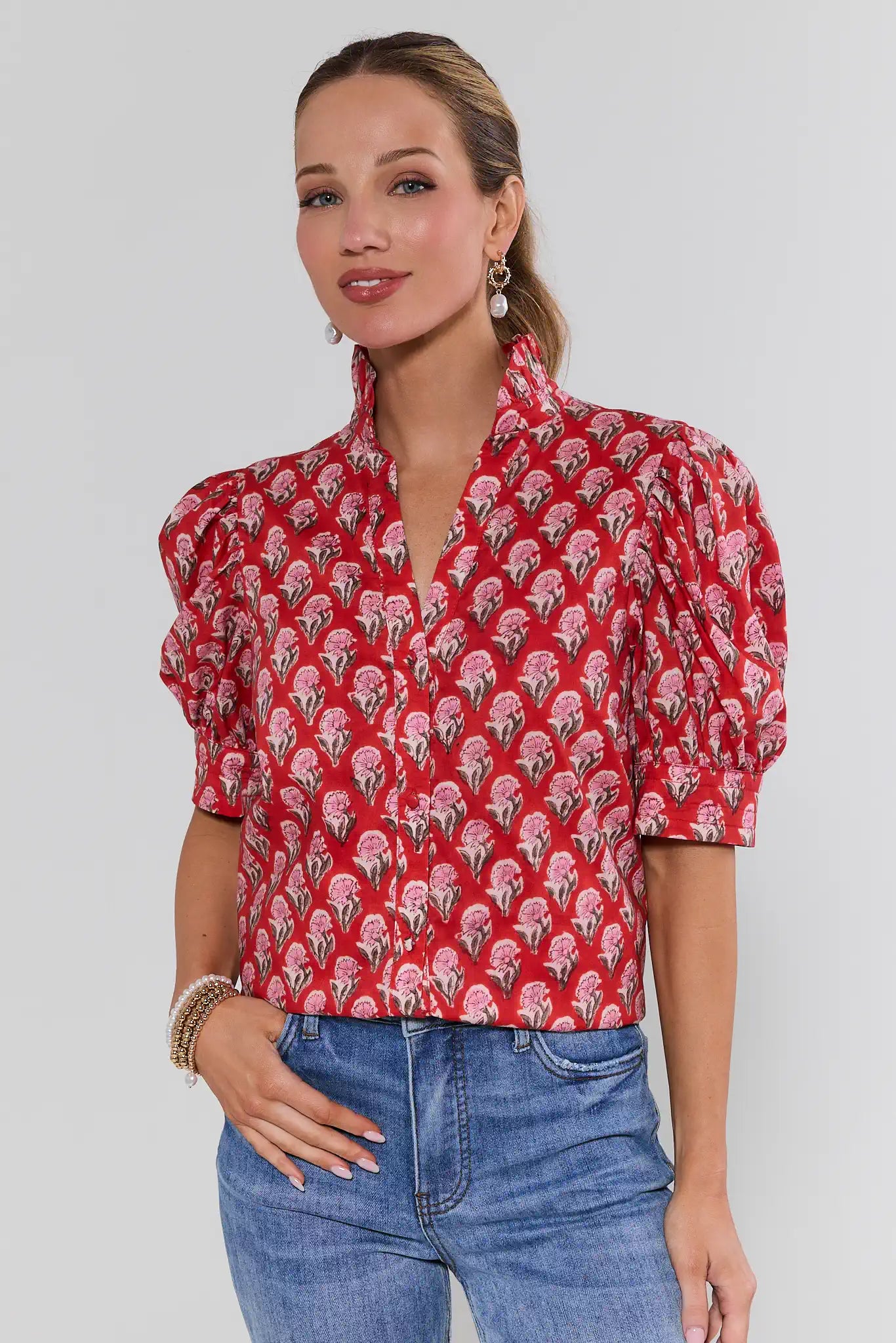Woman wearing a red patterned blouse and blue jeans against a white background