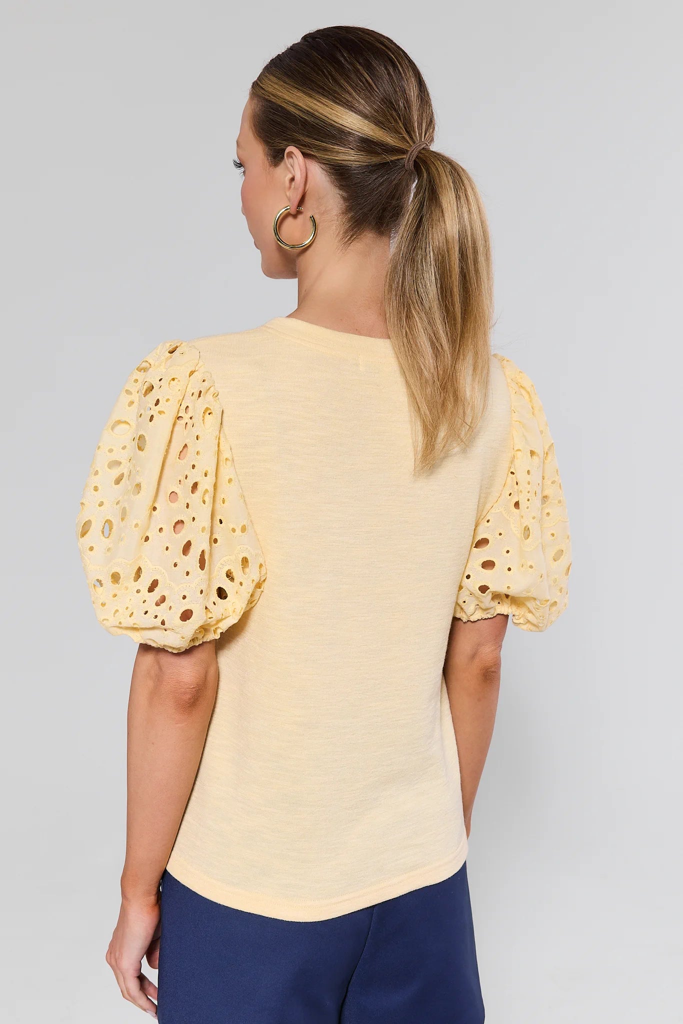 Woman wearing a yellow blouse with puff sleeves against a gray background