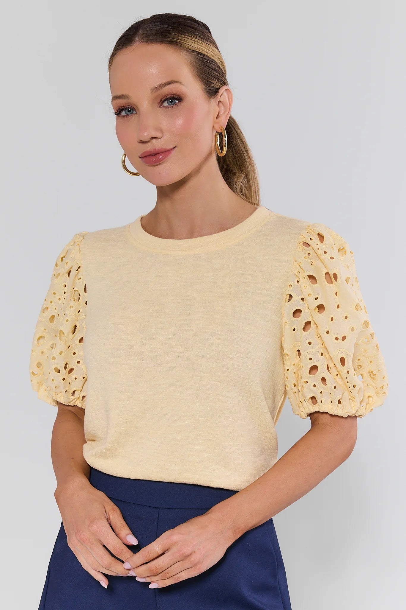 Woman wearing a yellow top with lace sleeves against a plain background