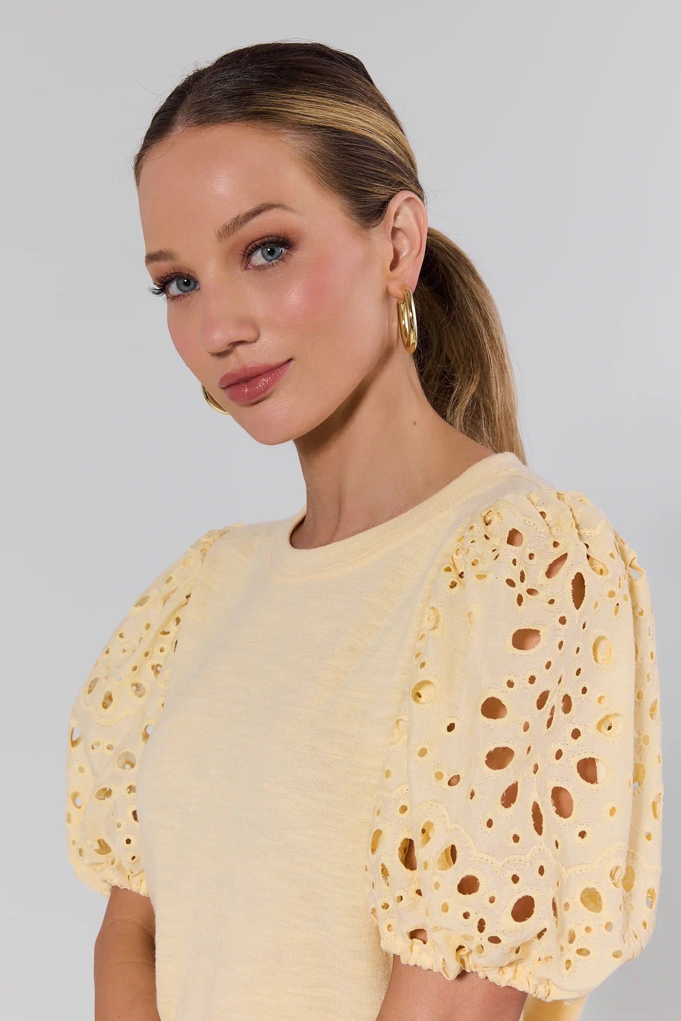 Woman wearing a yellow lace top against a plain background