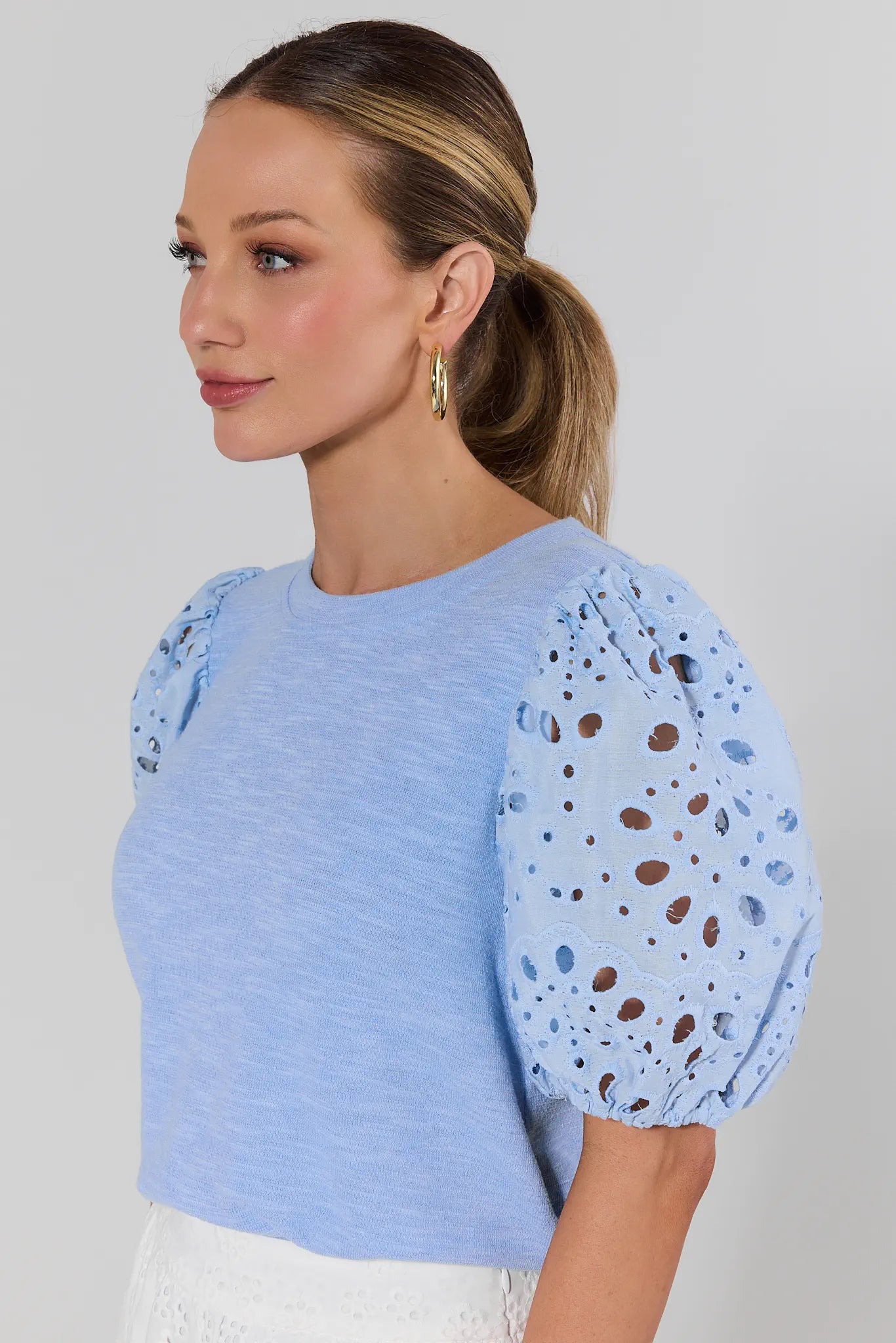 Woman wearing a light blue top with patterned sleeves against a plain background