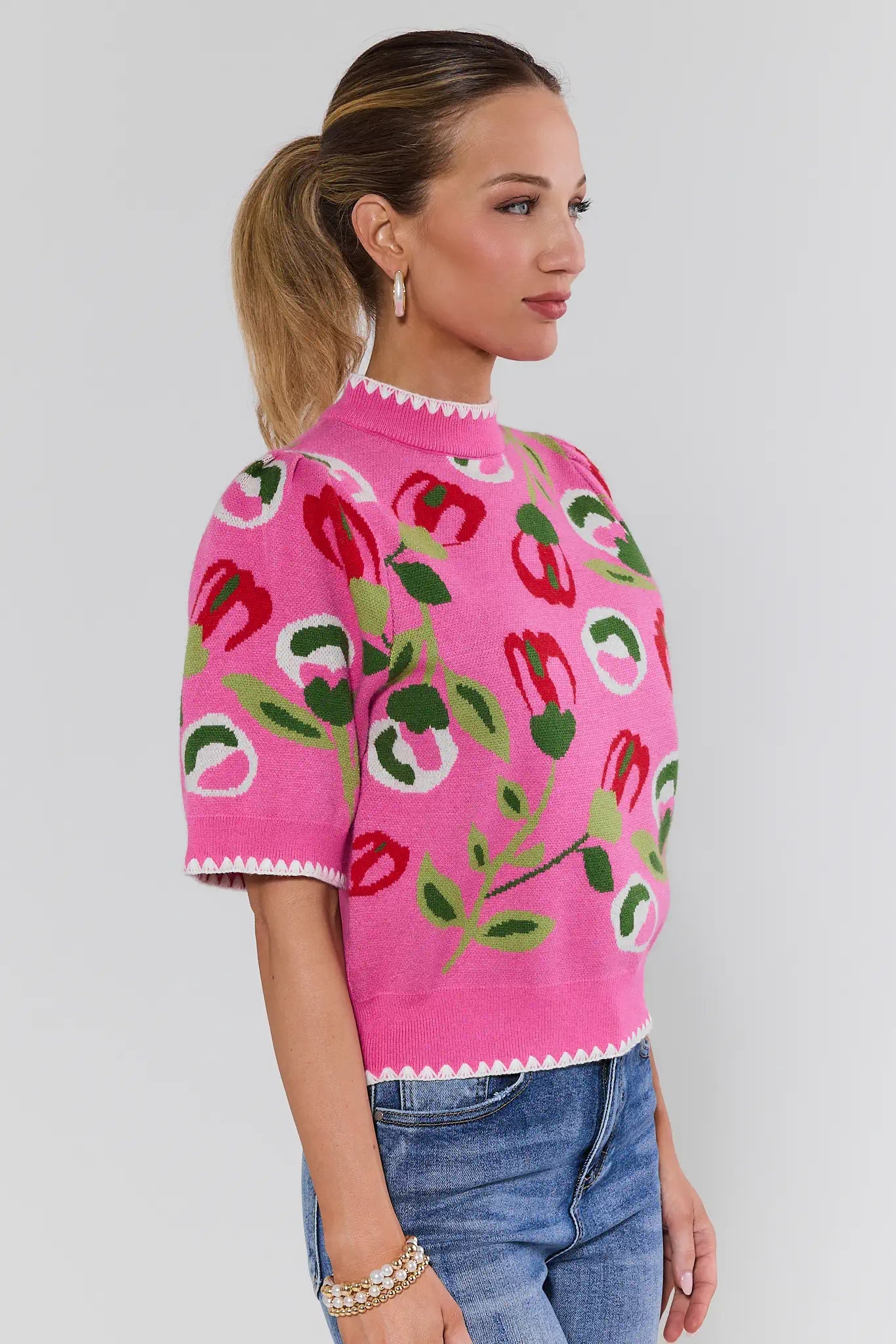 Woman wearing a pink sweater with floral patterns on a plain background