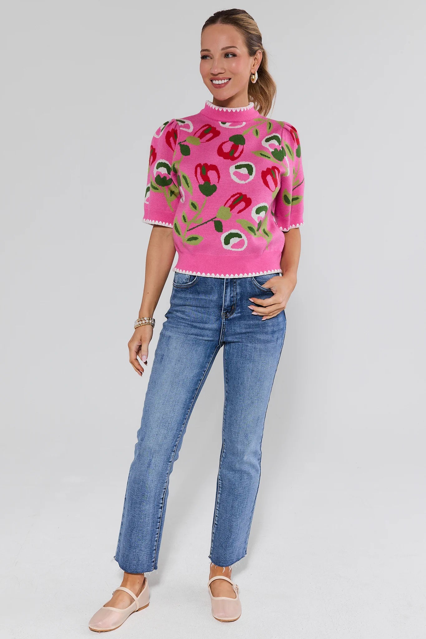Woman wearing a pink sweater with fruit pattern and blue jeans on a white background