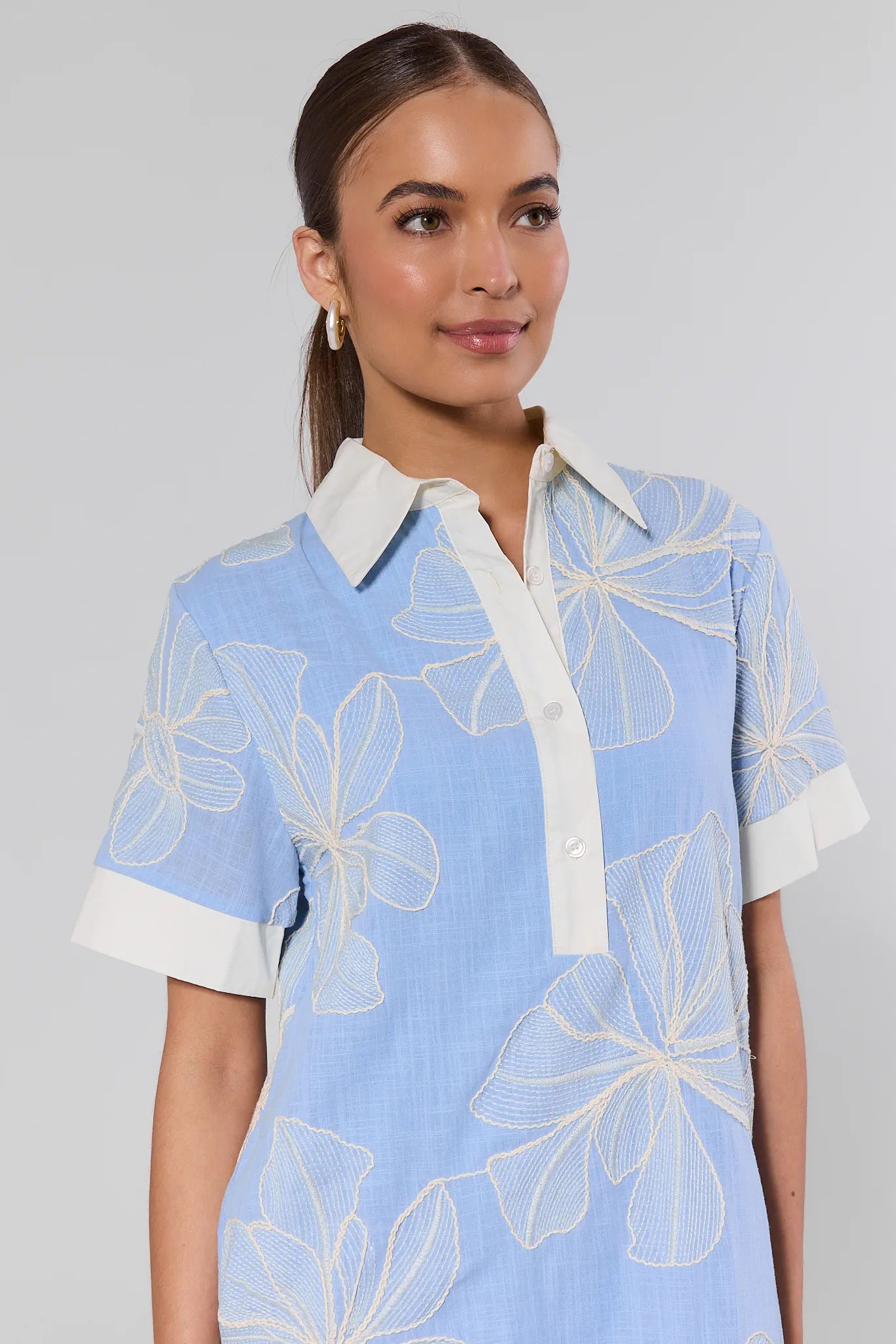 Woman wearing a light blue dress with white floral patterns on a gray background