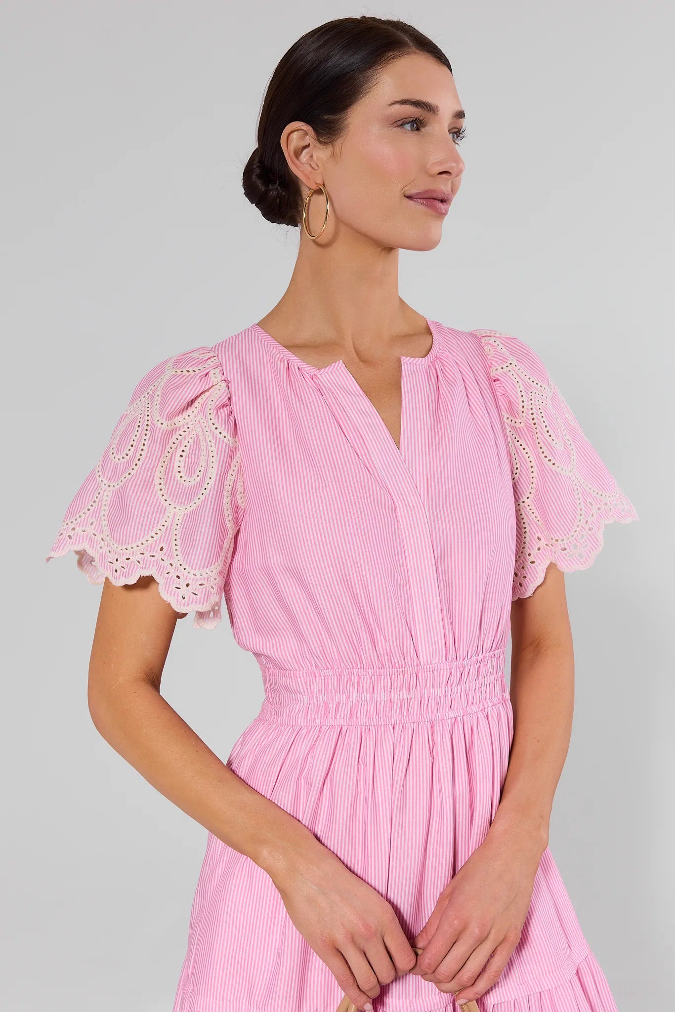 Woman wearing a pink dress with lace sleeves on a gray background