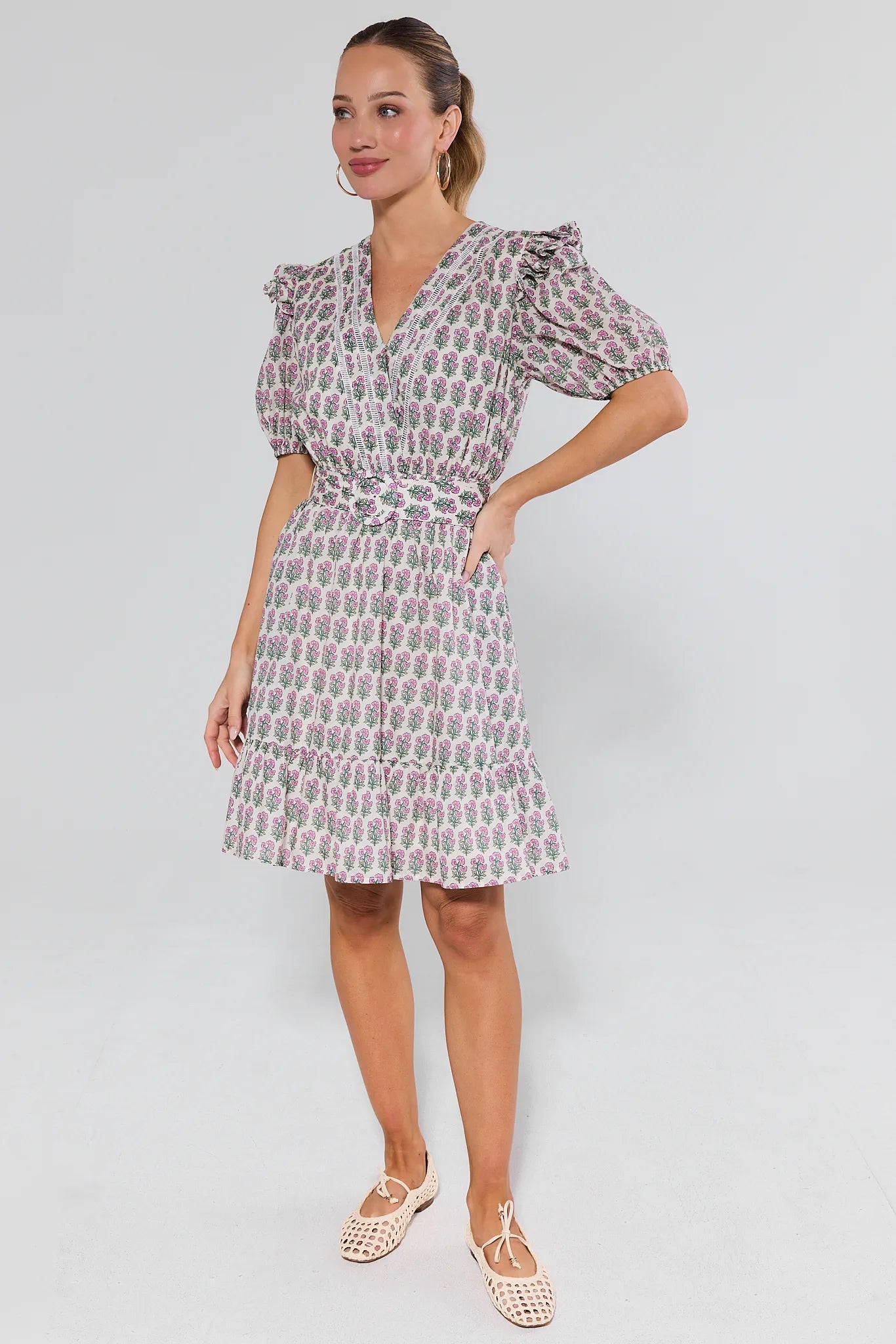 Woman wearing a patterned dress and flats on a plain background
