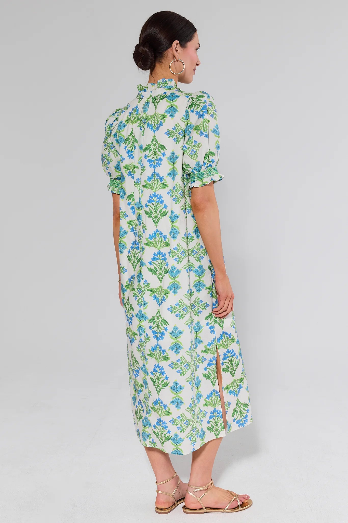 Woman standing wearing a floral dress on a plain background