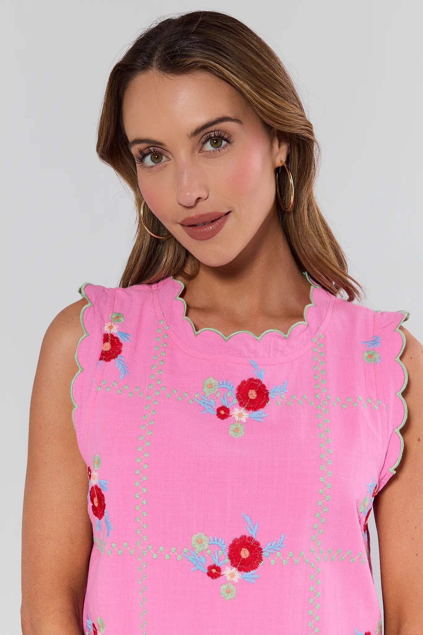 close up Woman wearing a pink dress with floral embroidery against a plain background