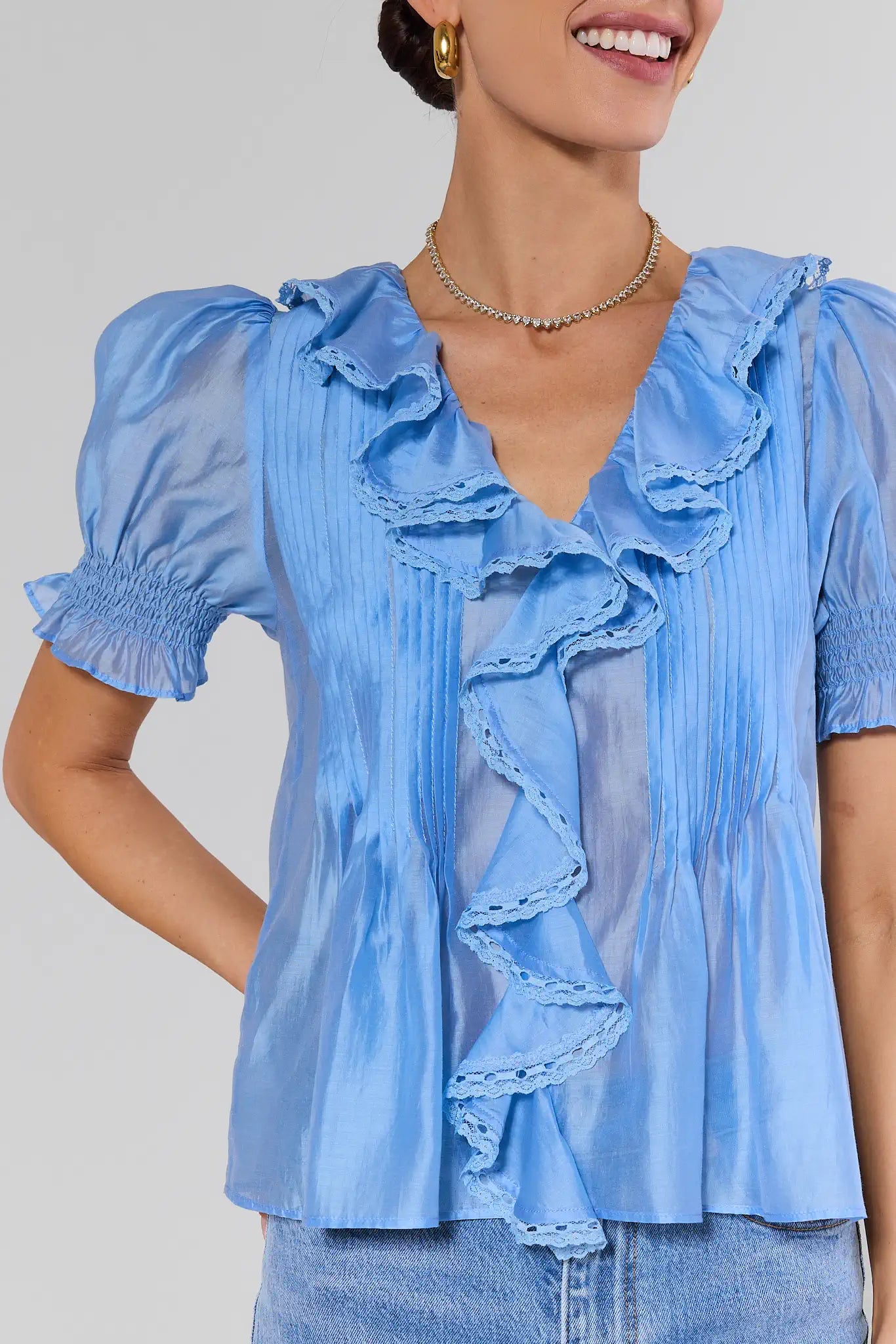 Woman wearing a blue blouse with ruffled details on a plain background