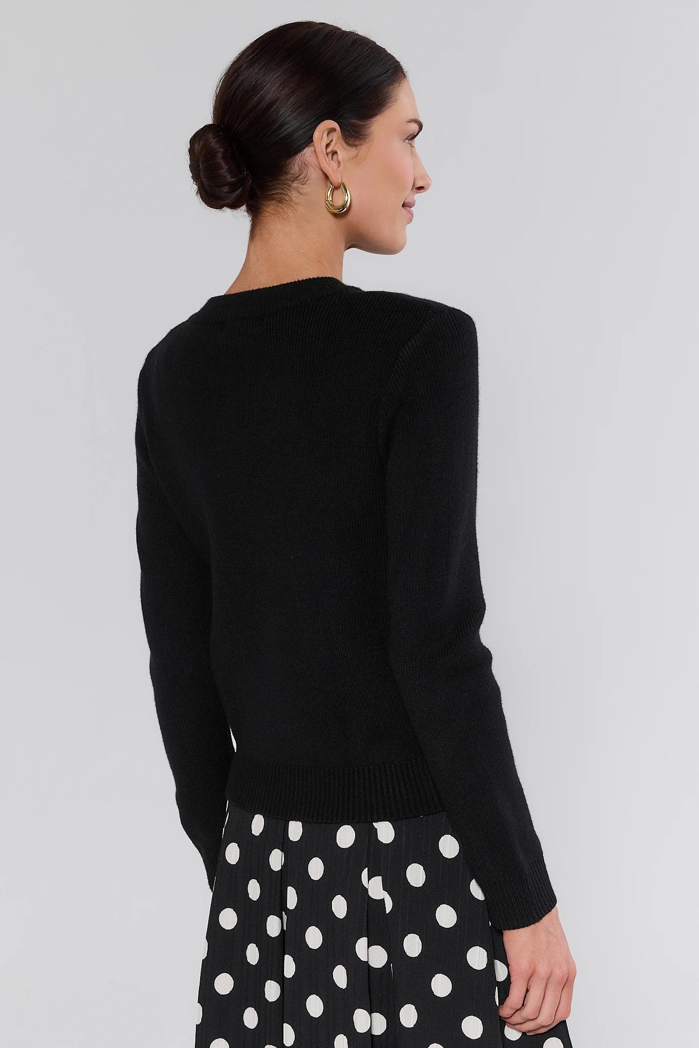 Woman wearing a black sweater and polka dot skirt on a plain background