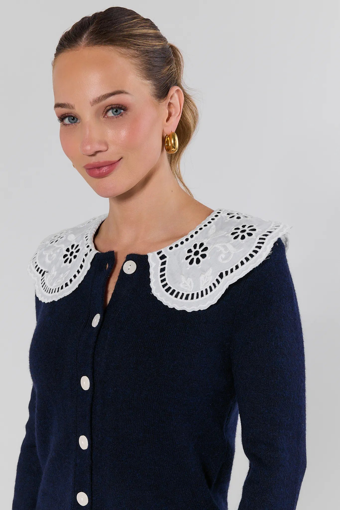 close up of Woman wearing a navy cardigan with white lace details on a plain background