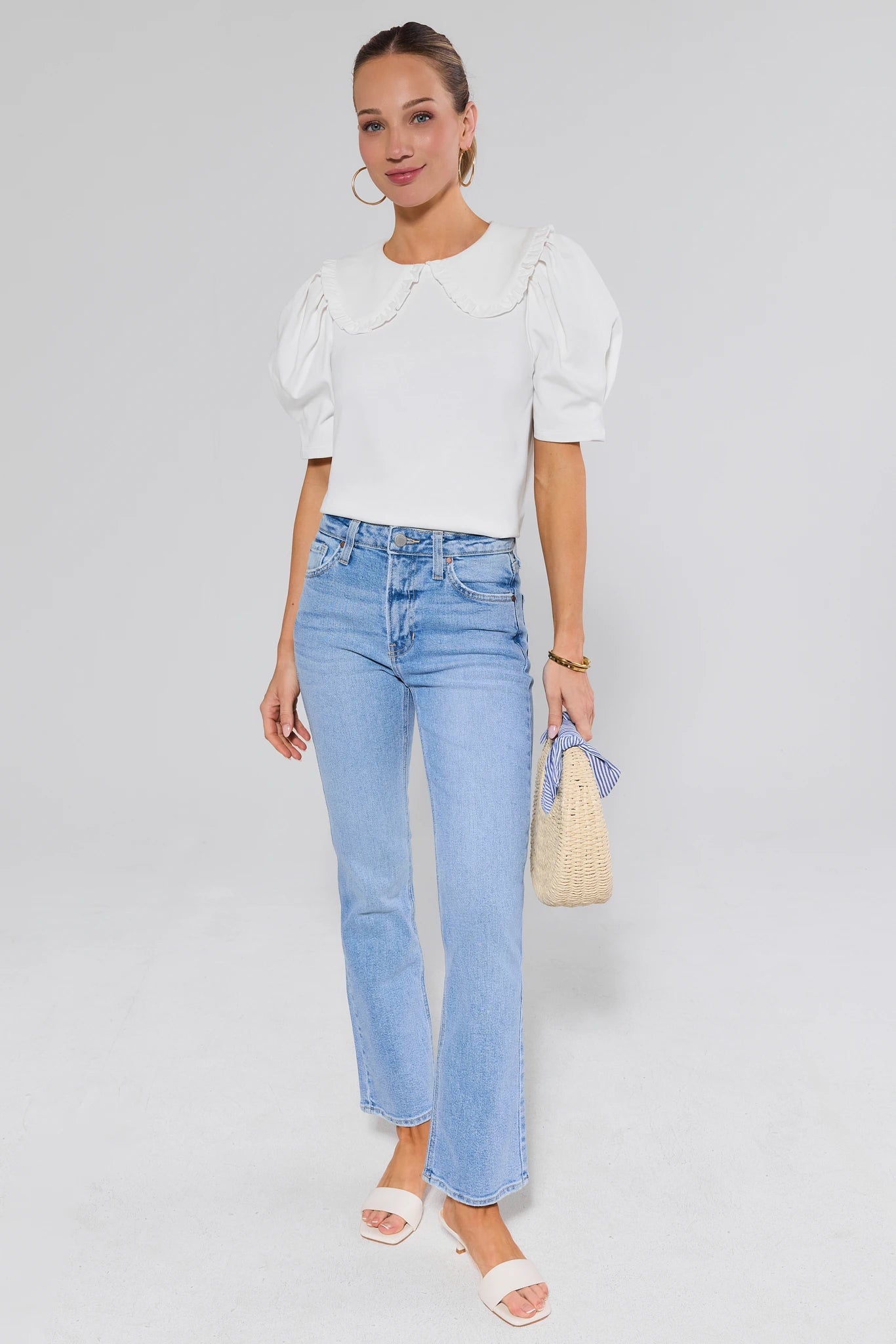 Woman wearing a white blouse and light blue jeans and heels on a plain background