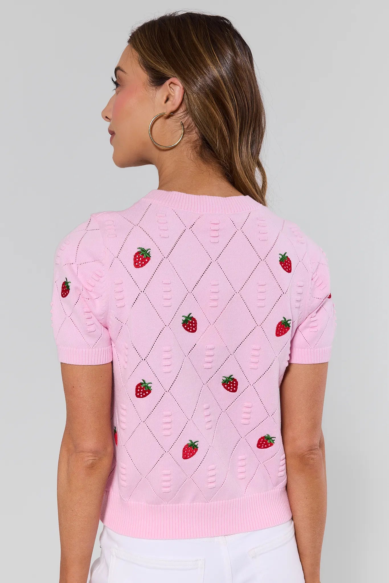 Woman wearing a pink sweater with strawberry patterns on a plain background
