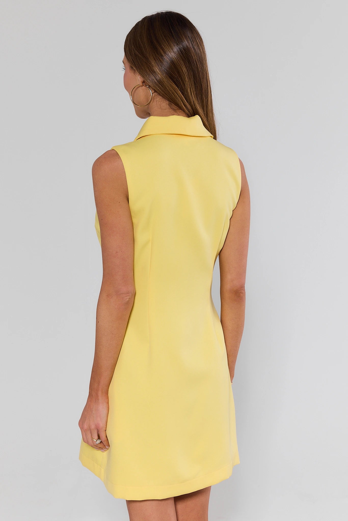 standing Woman wearing a yellow sleeveless dress against a plain background
