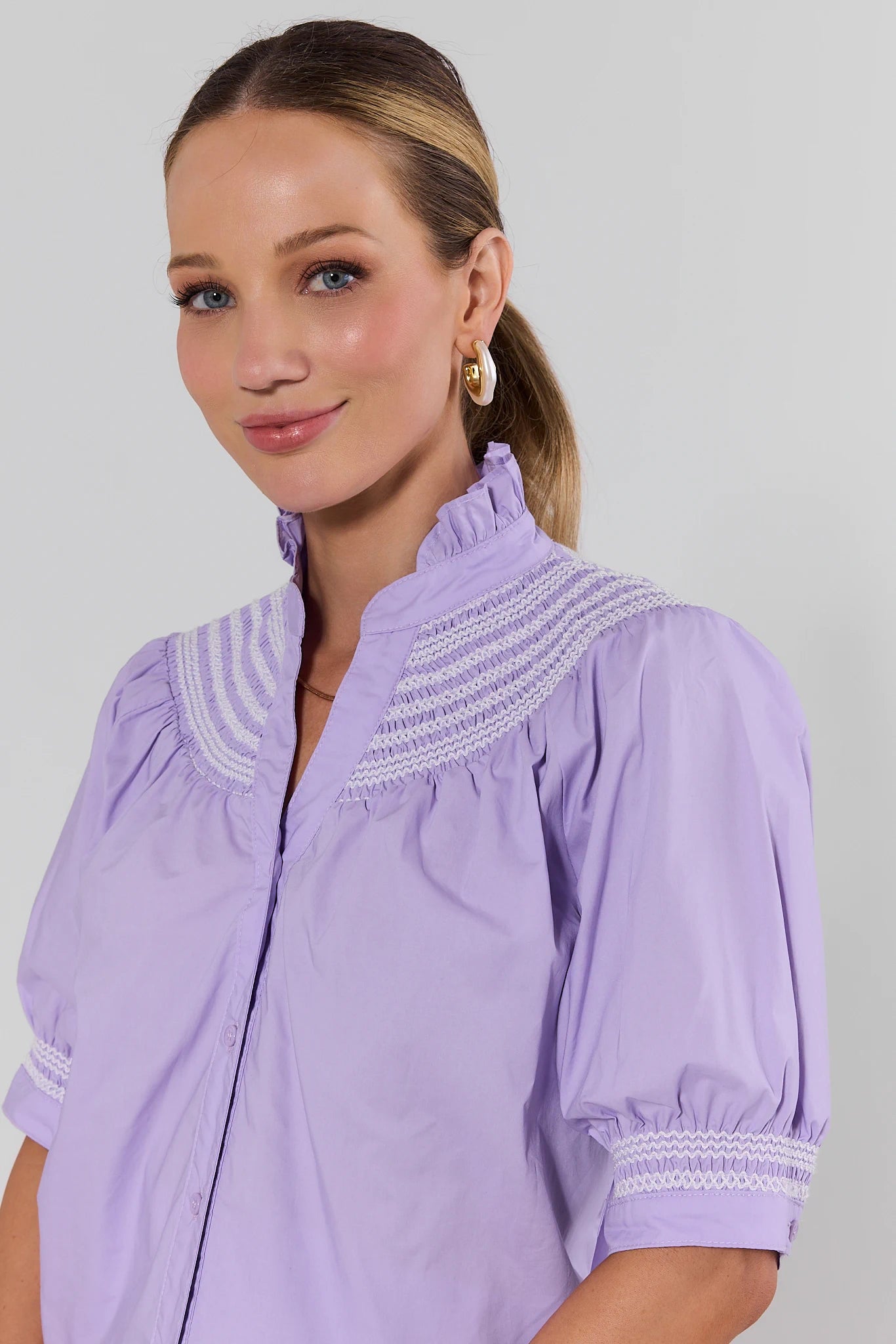 Woman wearing a light purple blouse with white embroidery on a plain background