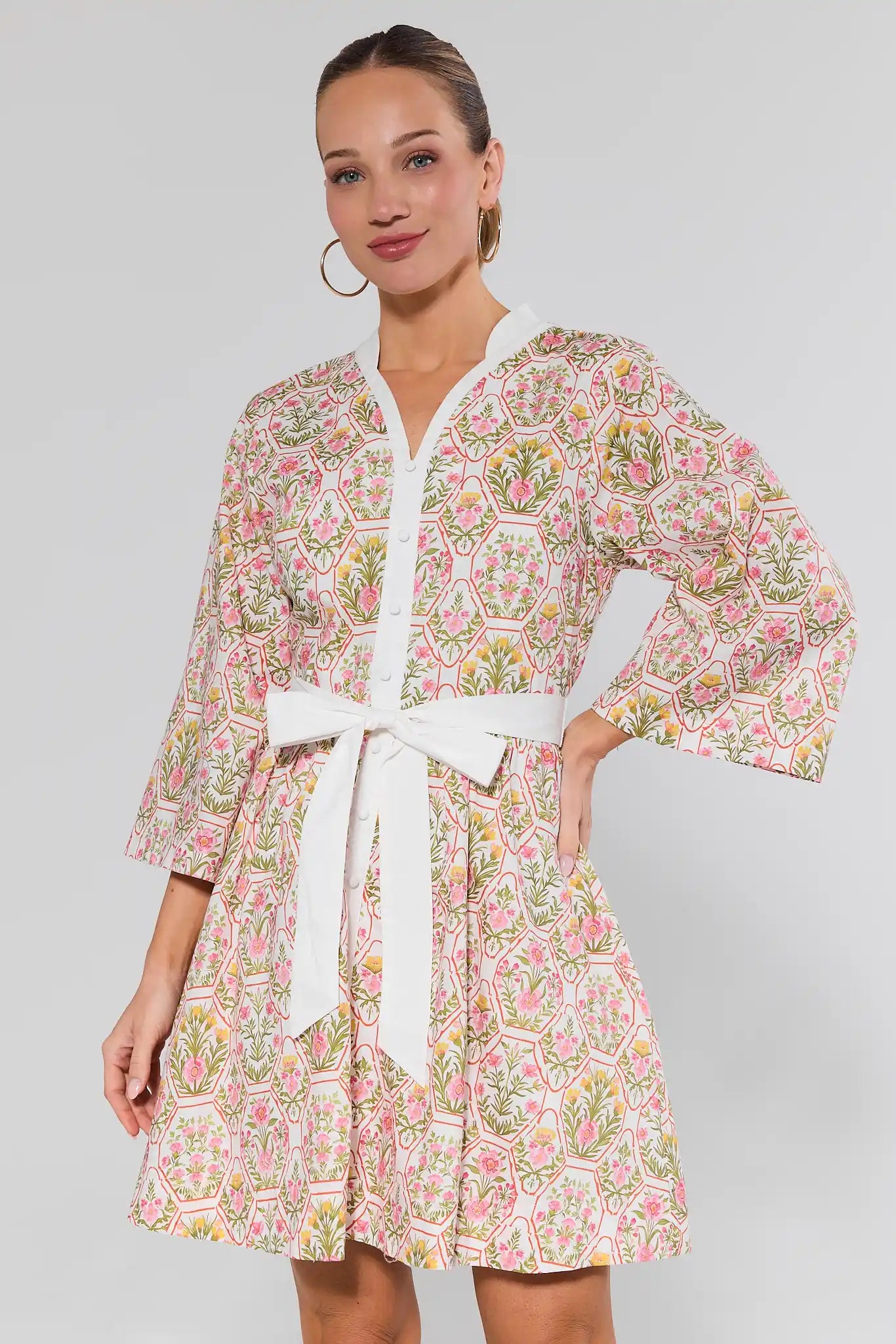 Woman wearing a floral dress with a white belt on a plain background