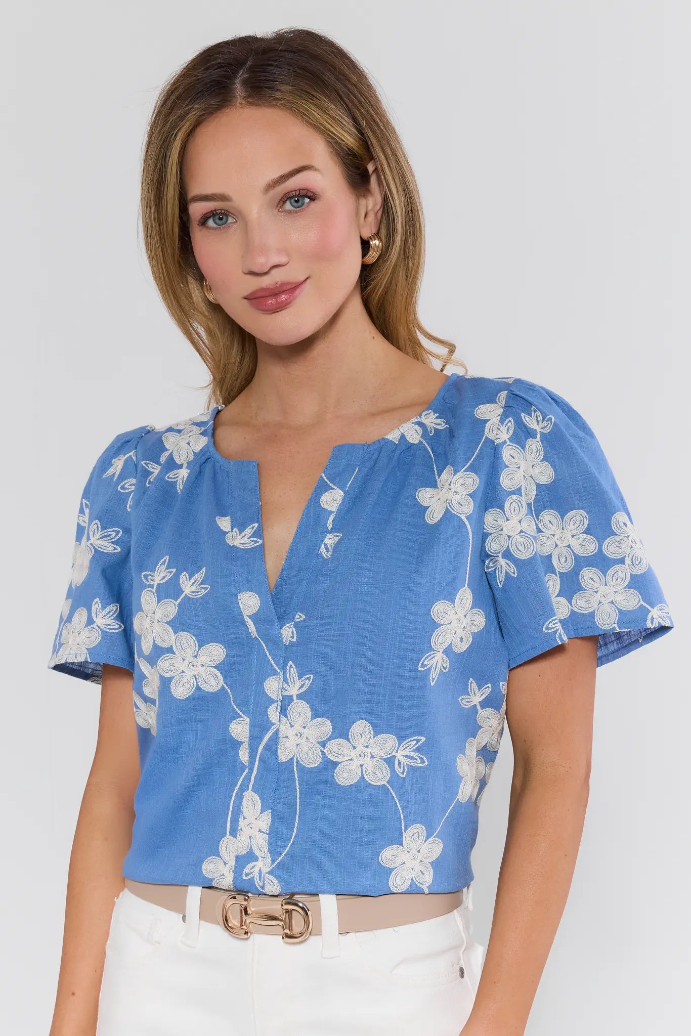 Cindy Blue Embroidered Short Sleeve Top with cream floral embroidery, V-neck, relaxed fit, worn by a woman with gold hoop earrings, showcasing elegant casual style.