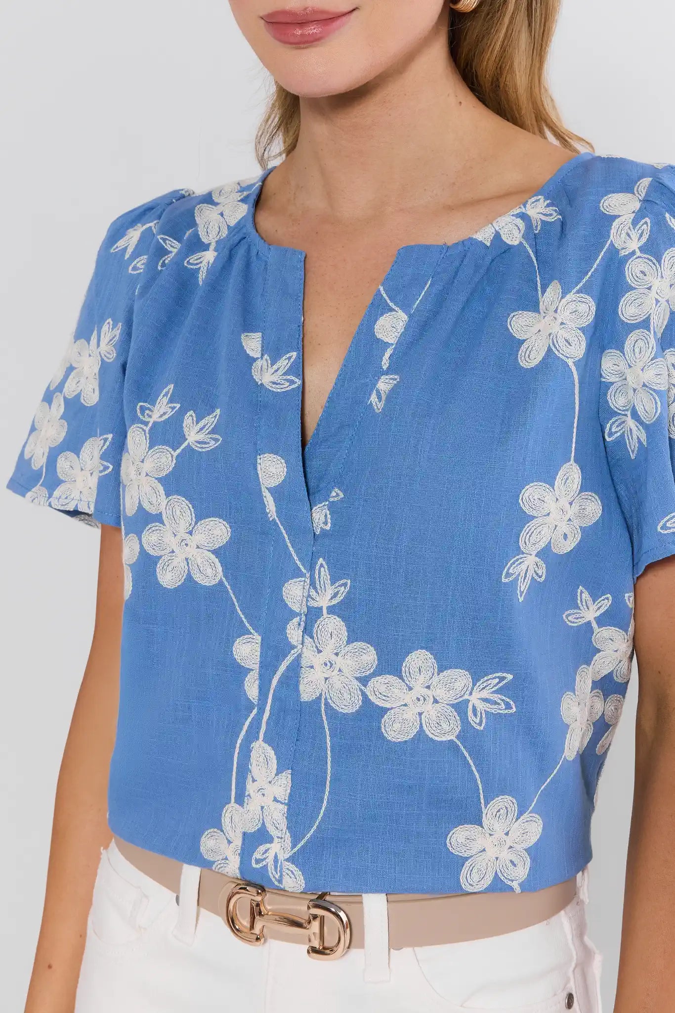 Cindy Blue Embroidered Short Sleeve Top with white floral embroidery, V-neckline, and relaxed fit, worn with high-waisted white pants and a beige belt.