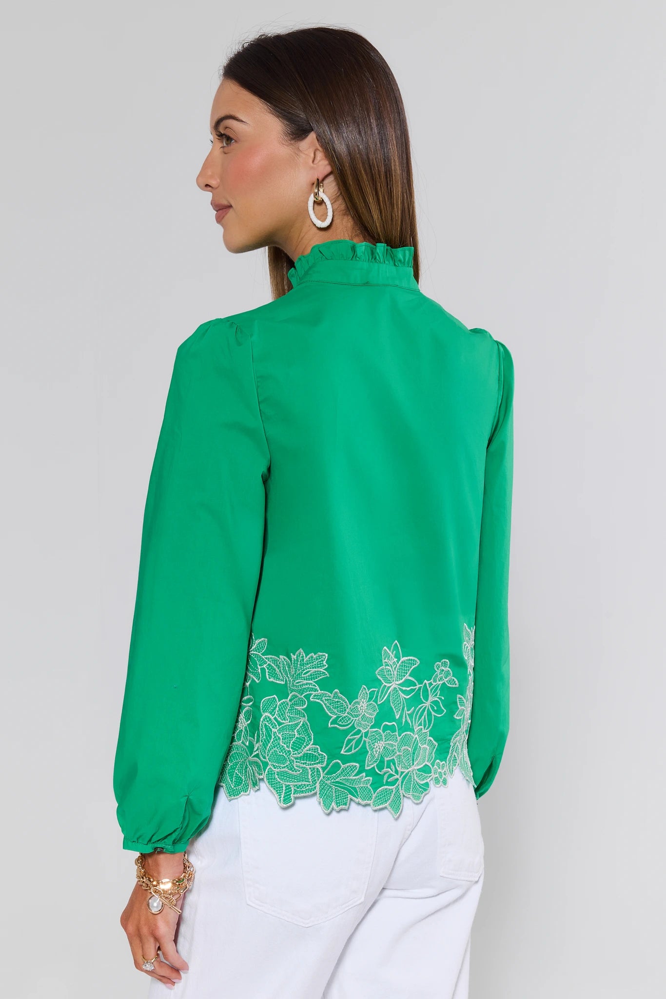 Woman wearing a green blouse with lace details on a plain background