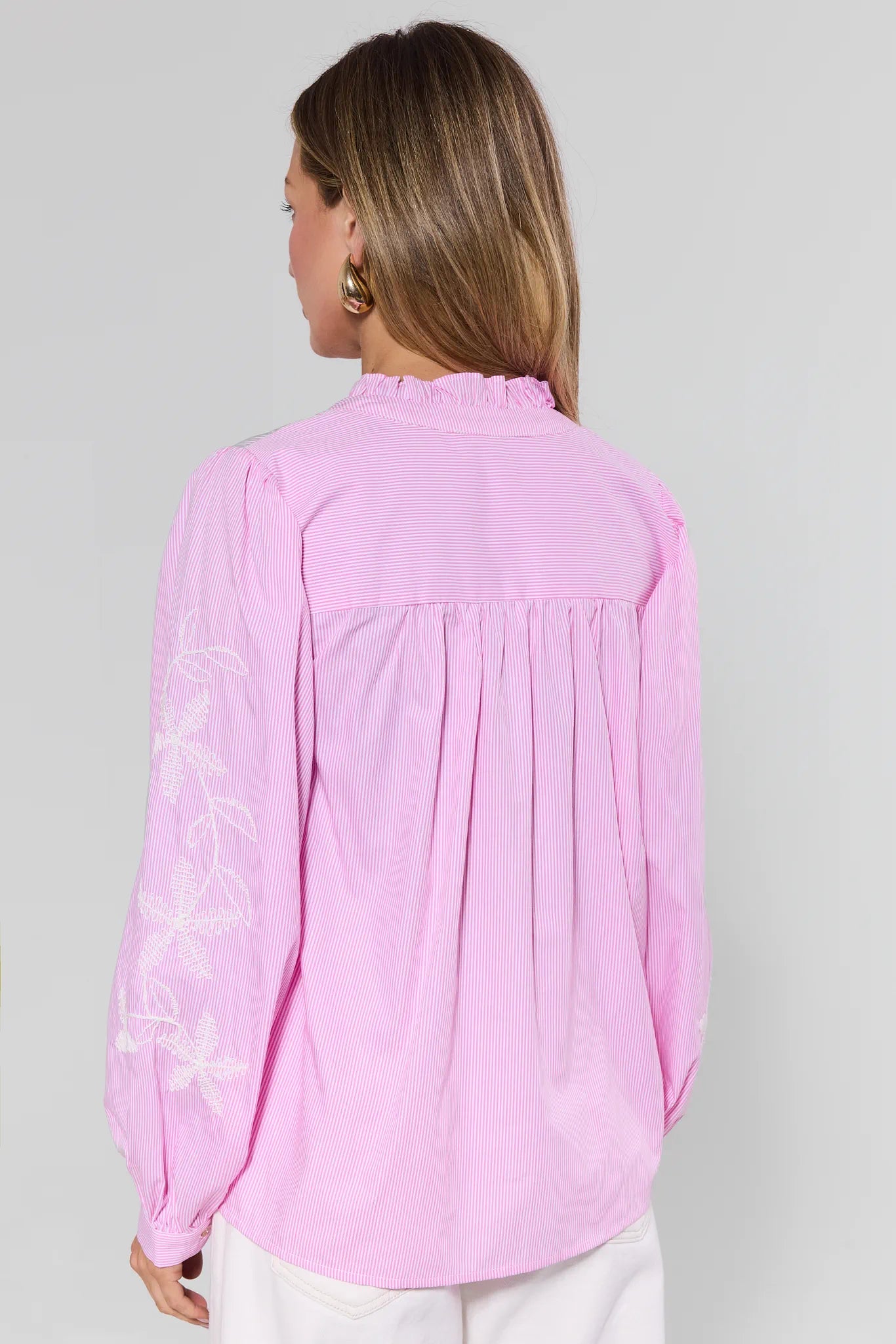 Woman wearing a pink blouse with floral embroidery on a gray background