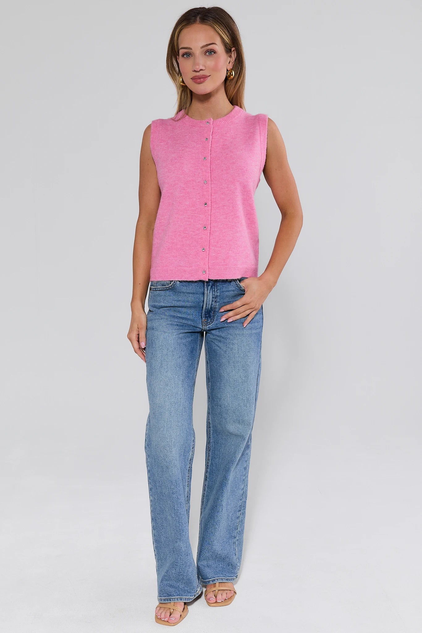 Woman wearing a pink sleeveless top and blue jeans on a white background