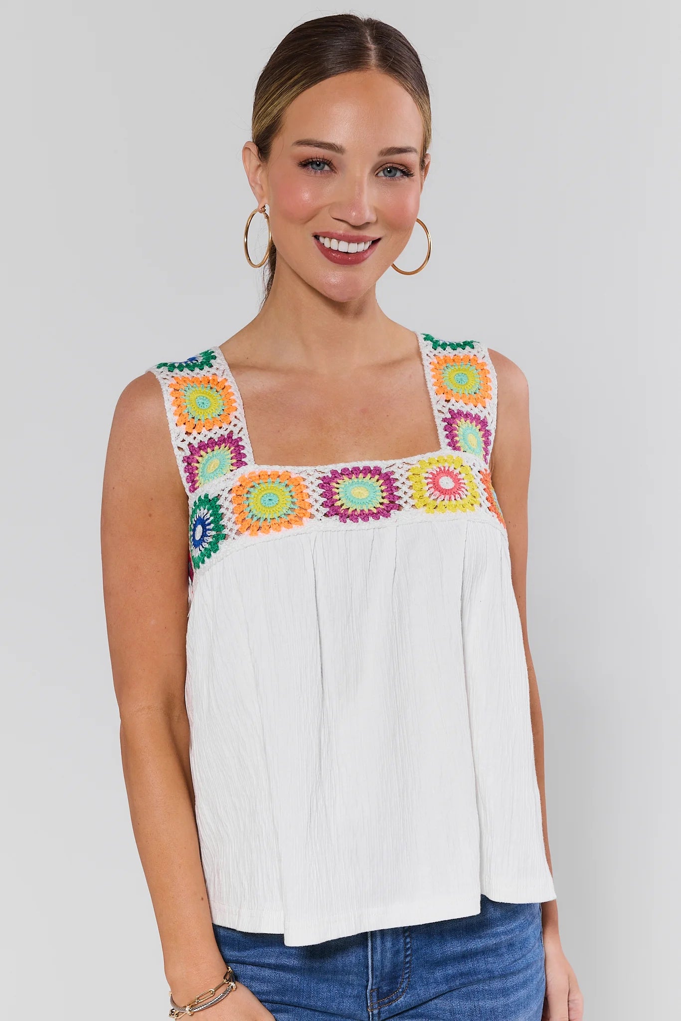 Woman wearing a white poppy top with colorful floral embroidery on a plain background