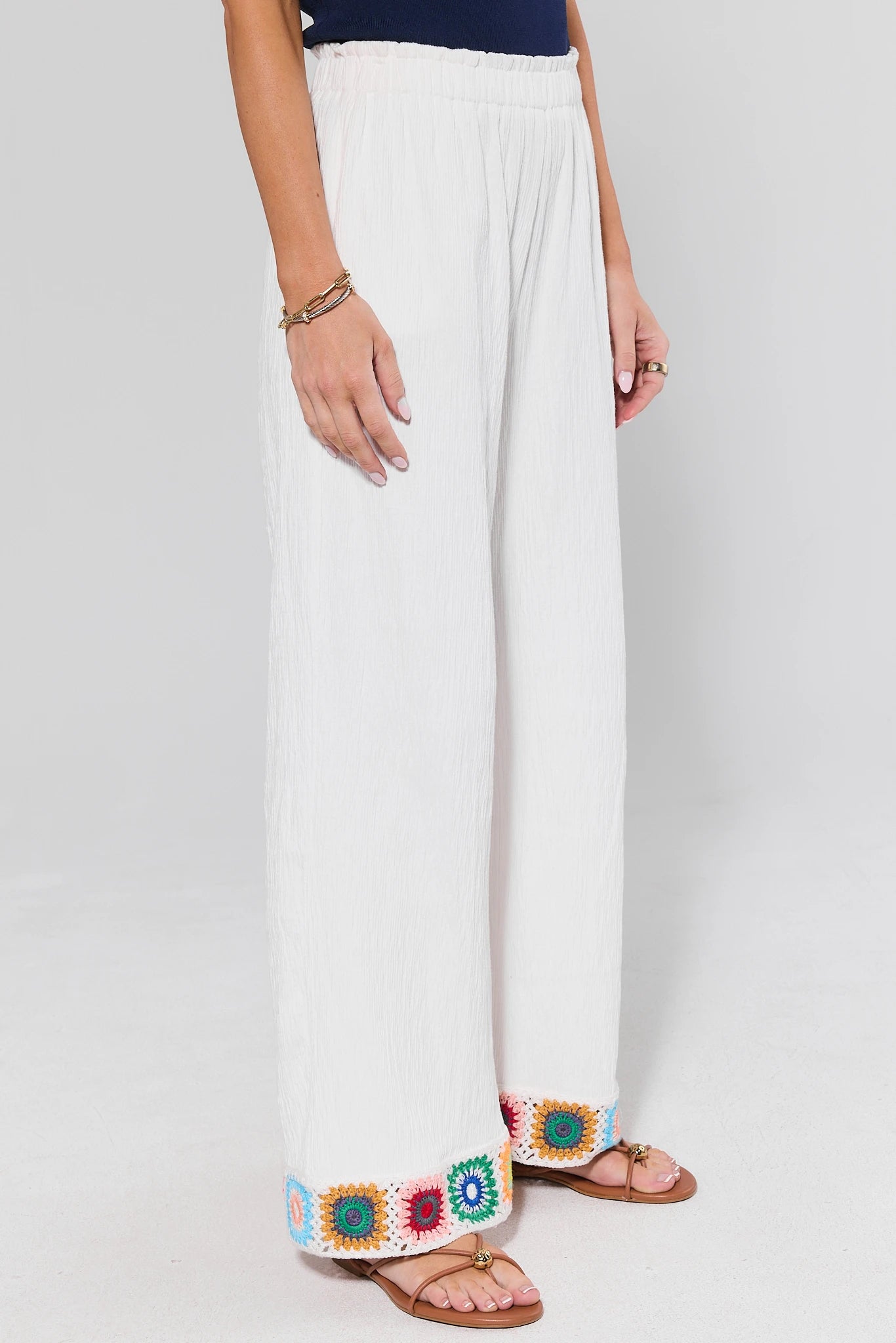 side shot Person wearing white pants and colorful sandals on a plain background
