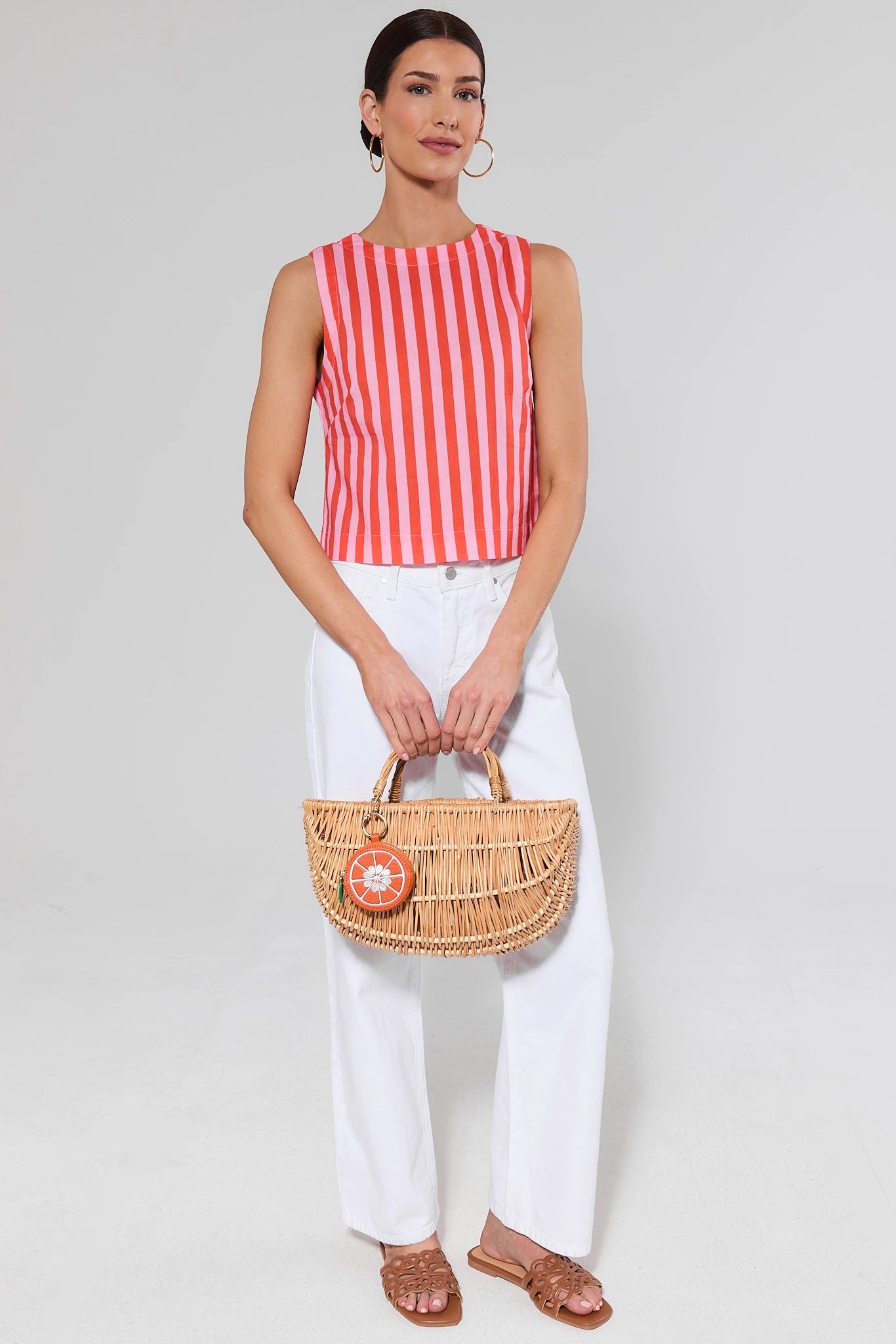 Woman wearing a red and white striped sleeveless top and white pants, holding a woven handbag.