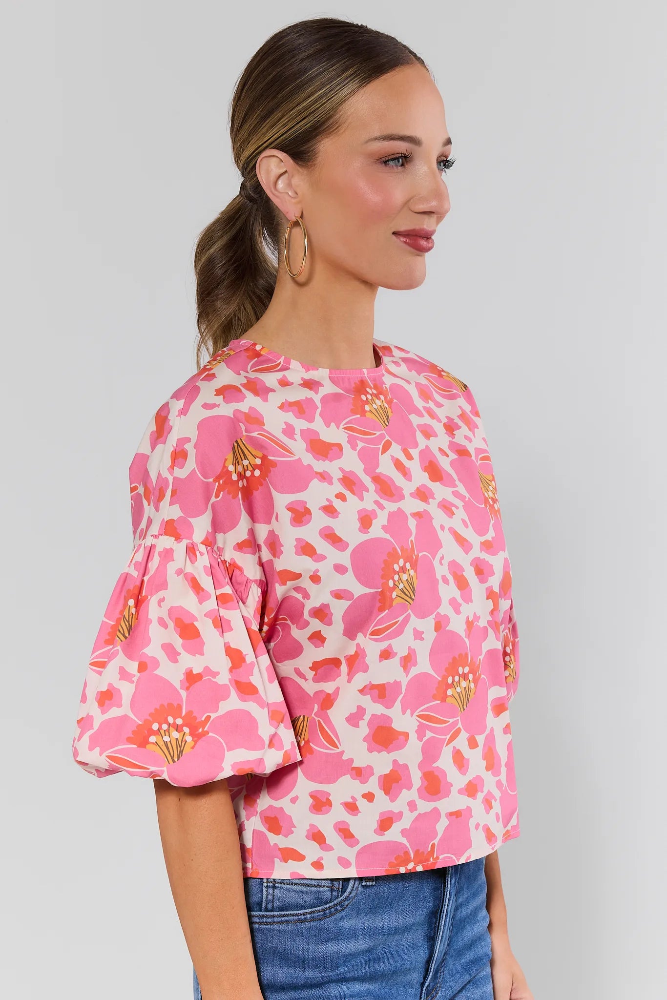 side shot Woman wearing a pink floral blouse against a plain background