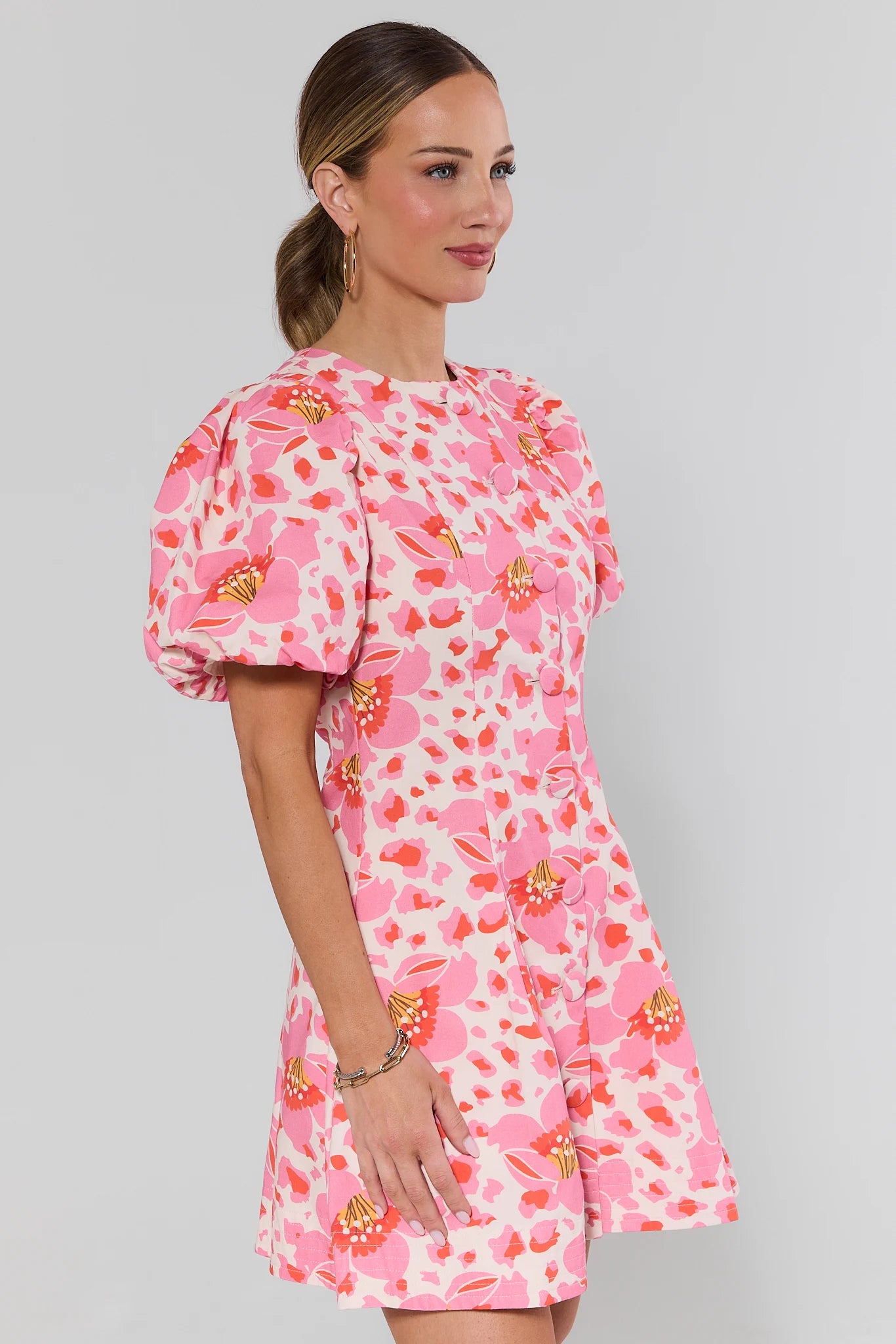 side shot Woman wearing a pink floral dress against a gray background