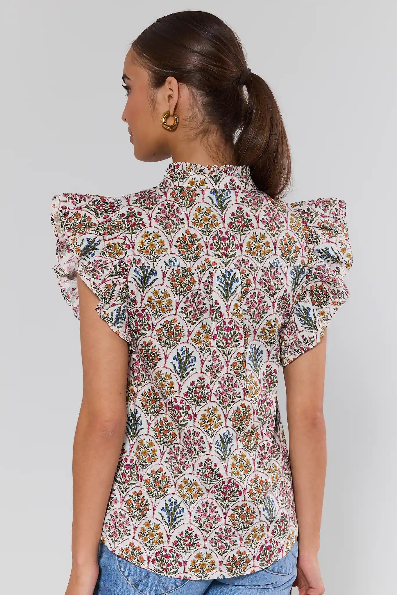 Woman wearing a floral patterned blouse with ruffled shoulders on a plain background